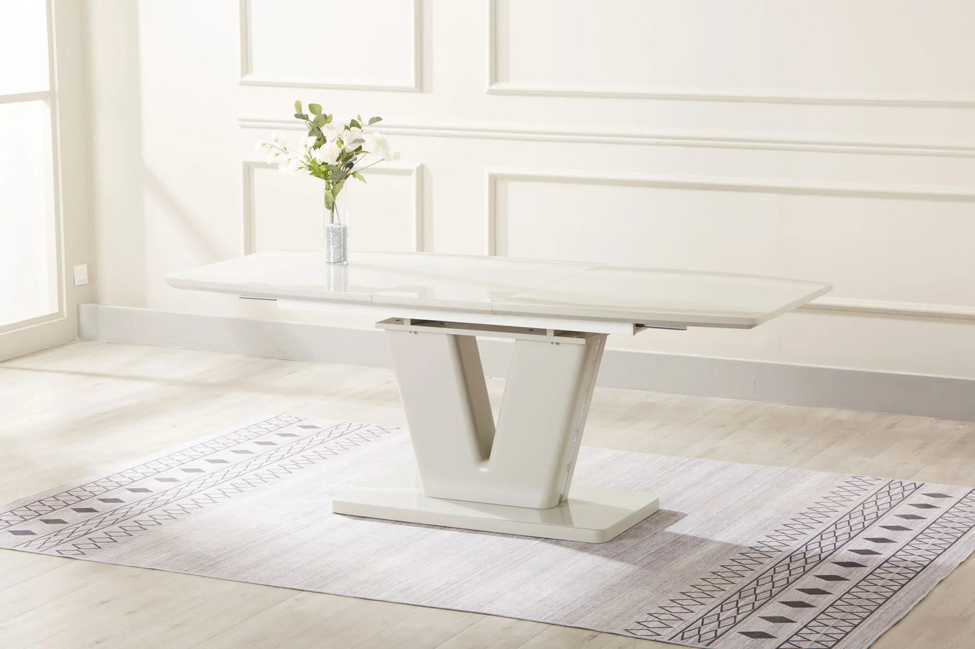 Gloss white extension dining table with V-shaped base on patterned rug in bright room