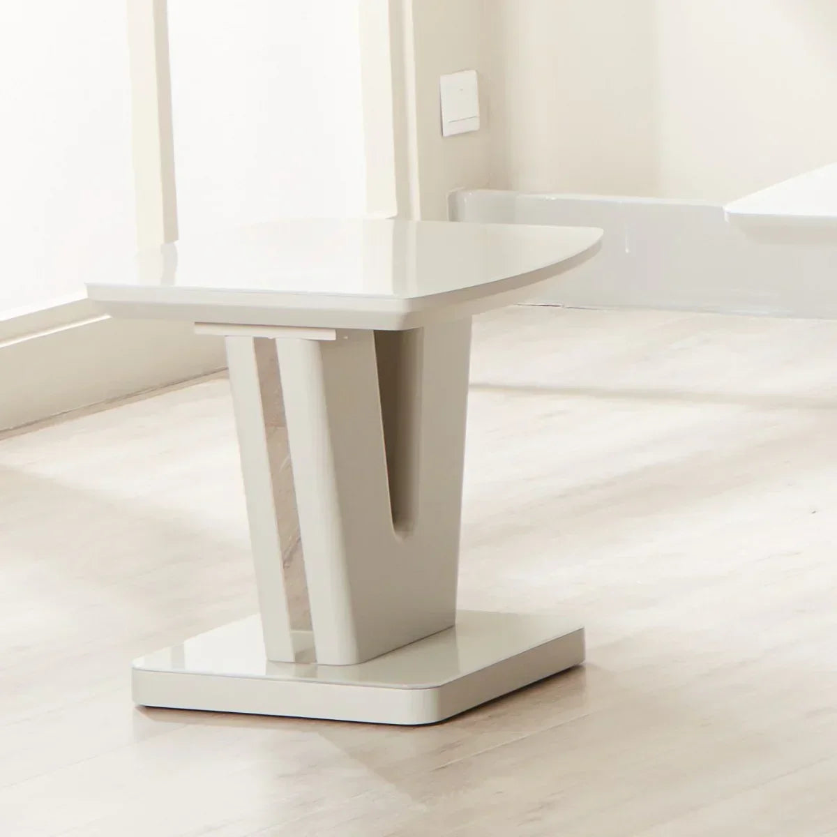 Glossy cream lamp table with V-shaped base on light wood floor