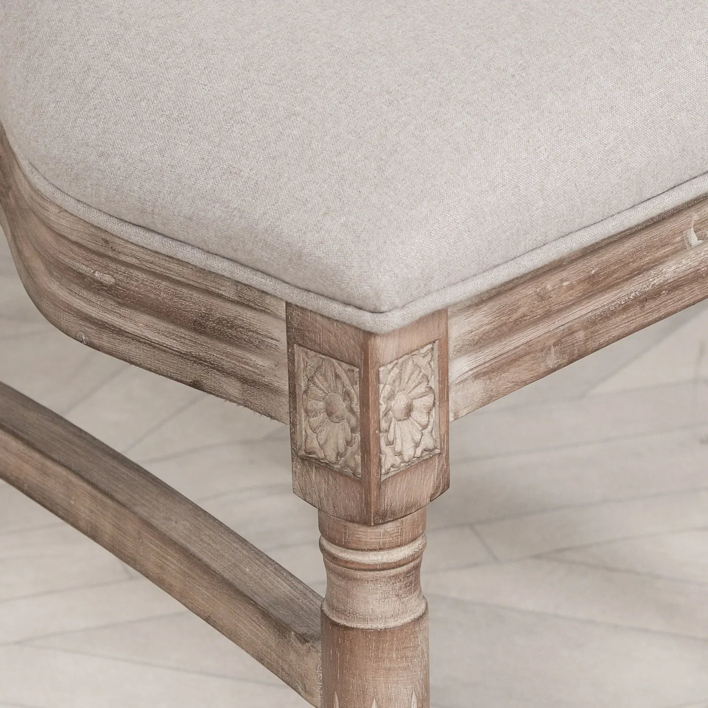 Closeup of wooden dining chair leg with carved floral detail and linen seat cushion