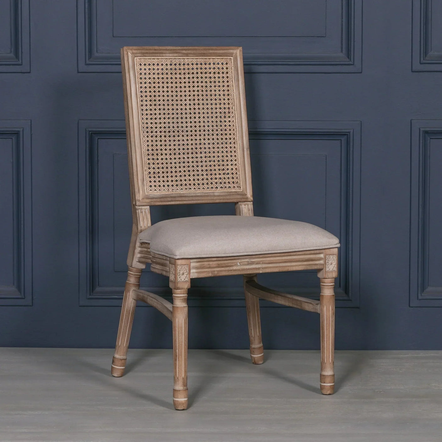 Wooden dining chair with cane backrest and light upholstered seat against a navy wall