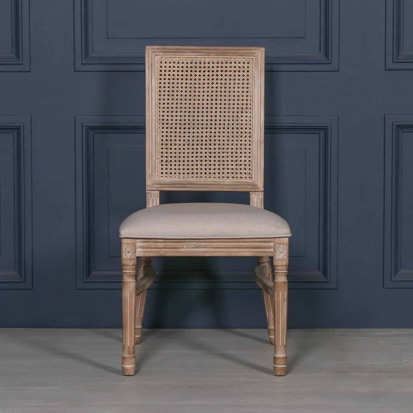 Wooden dining chair with cane backrest and beige upholstered seat against navy panel wall