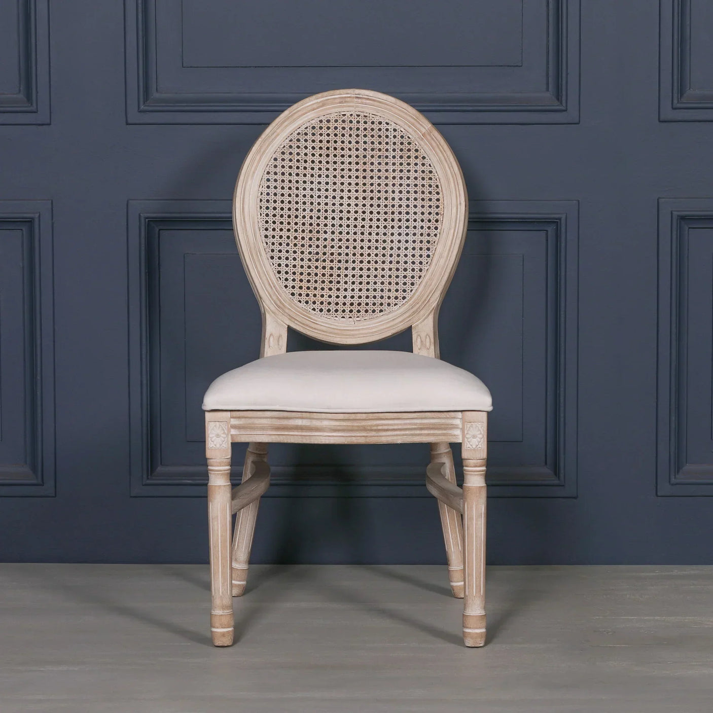 Beige rattan dining chair with round cane back and cushioned seat against navy wall