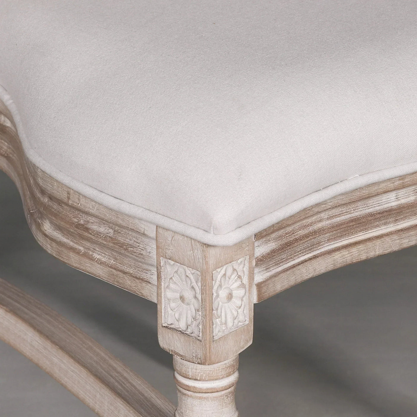 Close-up of carved wooden dining chair leg with white upholstered seat cushion