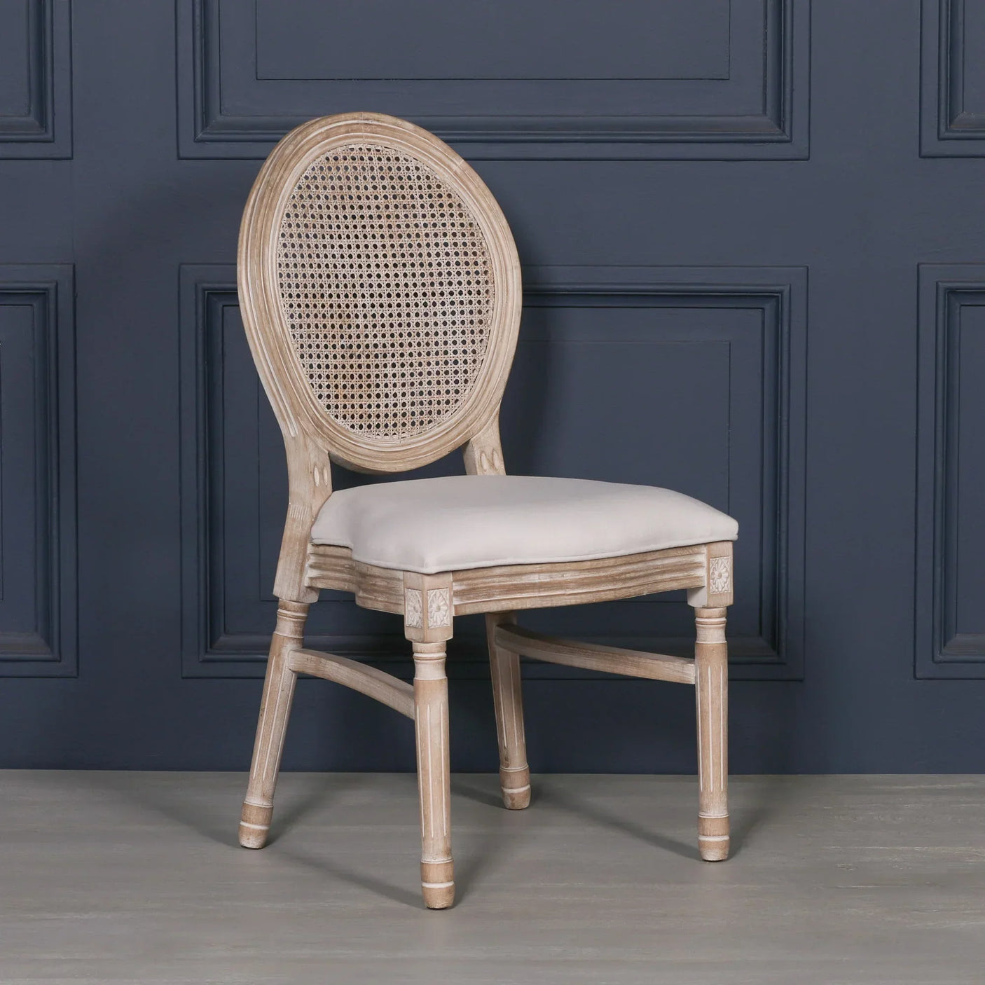 Wooden dining chair with cane oval backrest and cream cushioned seat against dark wall