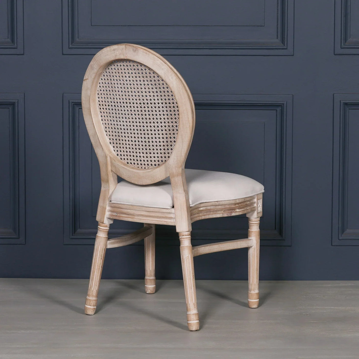 Wooden dining chair with oval rattan back and upholstered seat, angled rear view