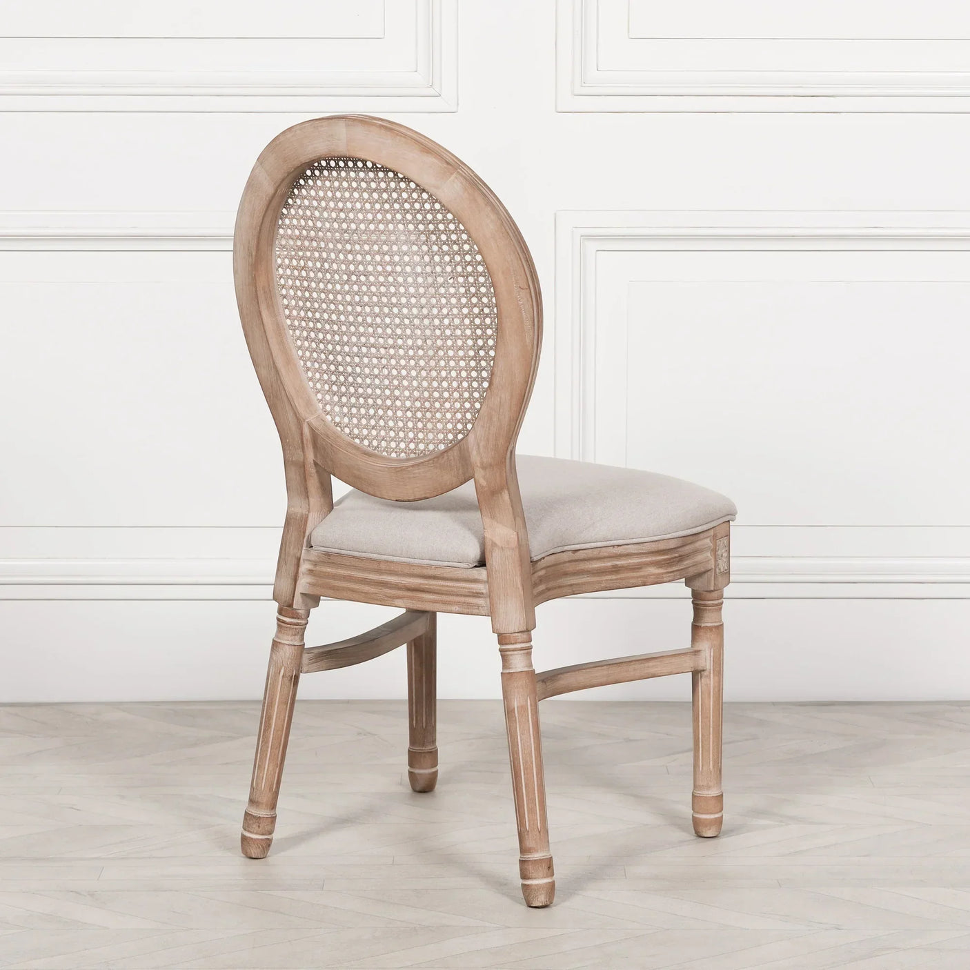 Oak dining chair with oval cane back and beige upholstered seat on wood floor