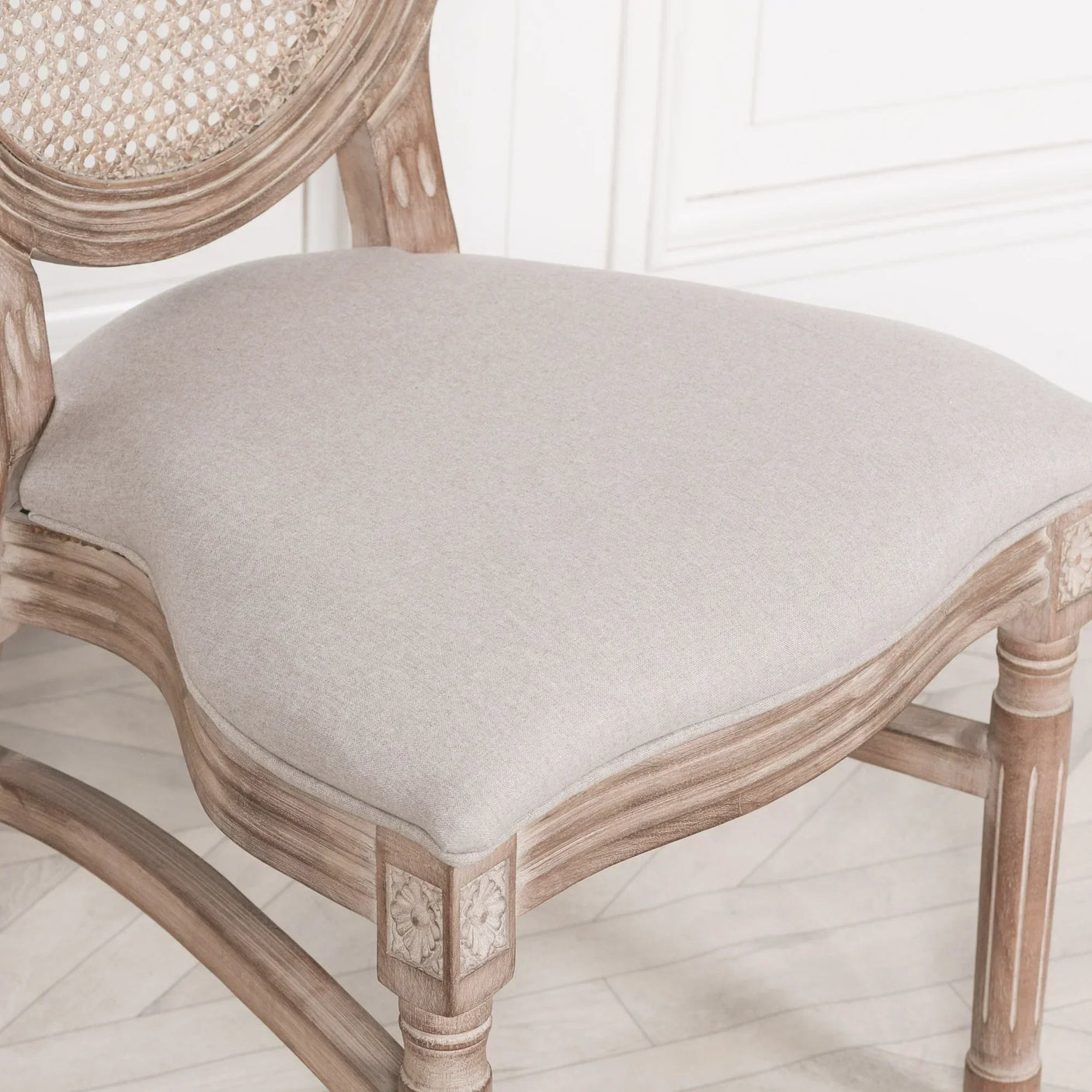Beige upholstered dining chair with weathered wood frame and carved floral detailing