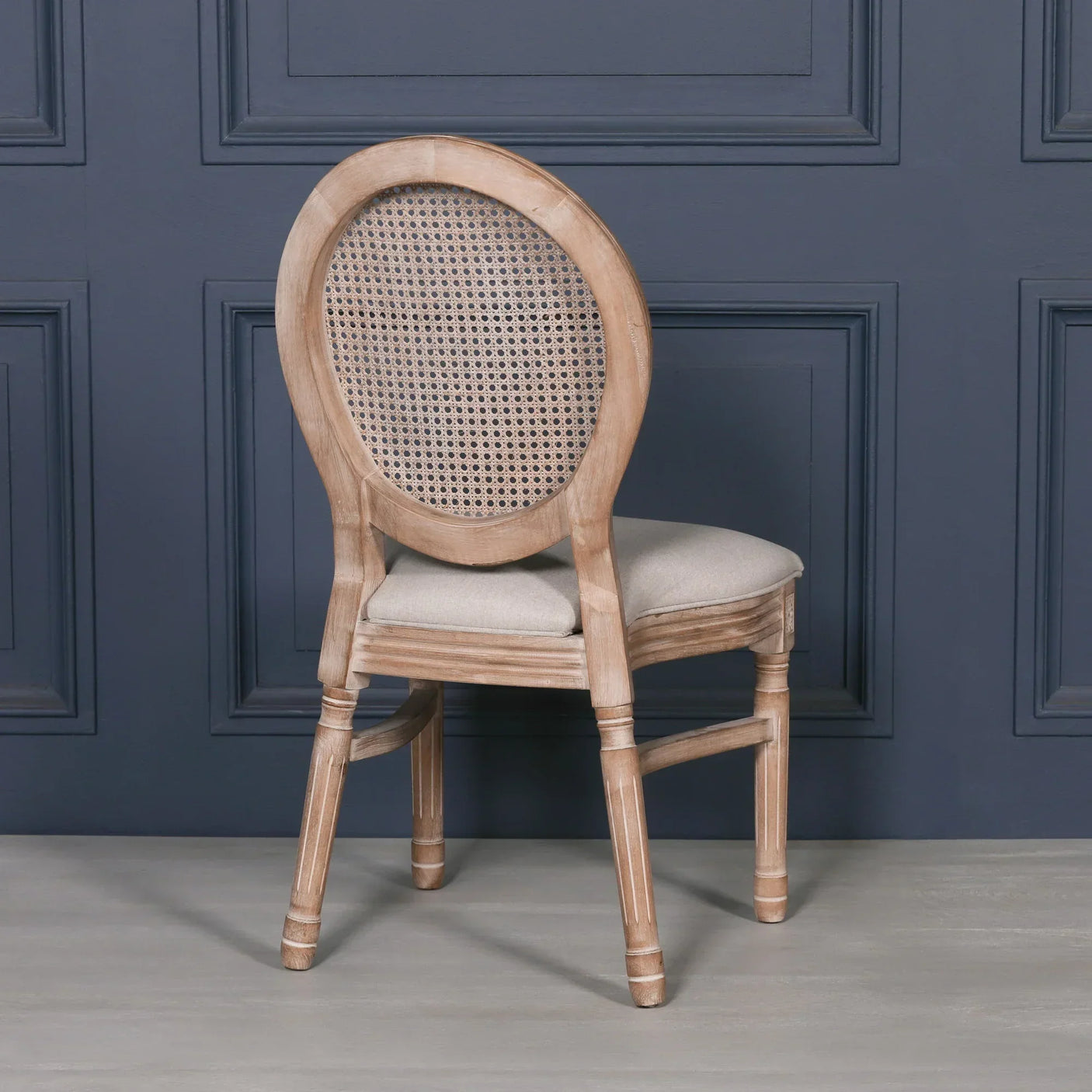 Oak dining chair with oval cane back and beige upholstered seat on wooden floor
