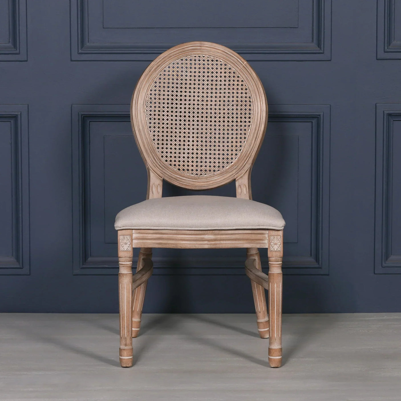 Wooden dining chair with round cane backrest and beige upholstered seat against blue wall