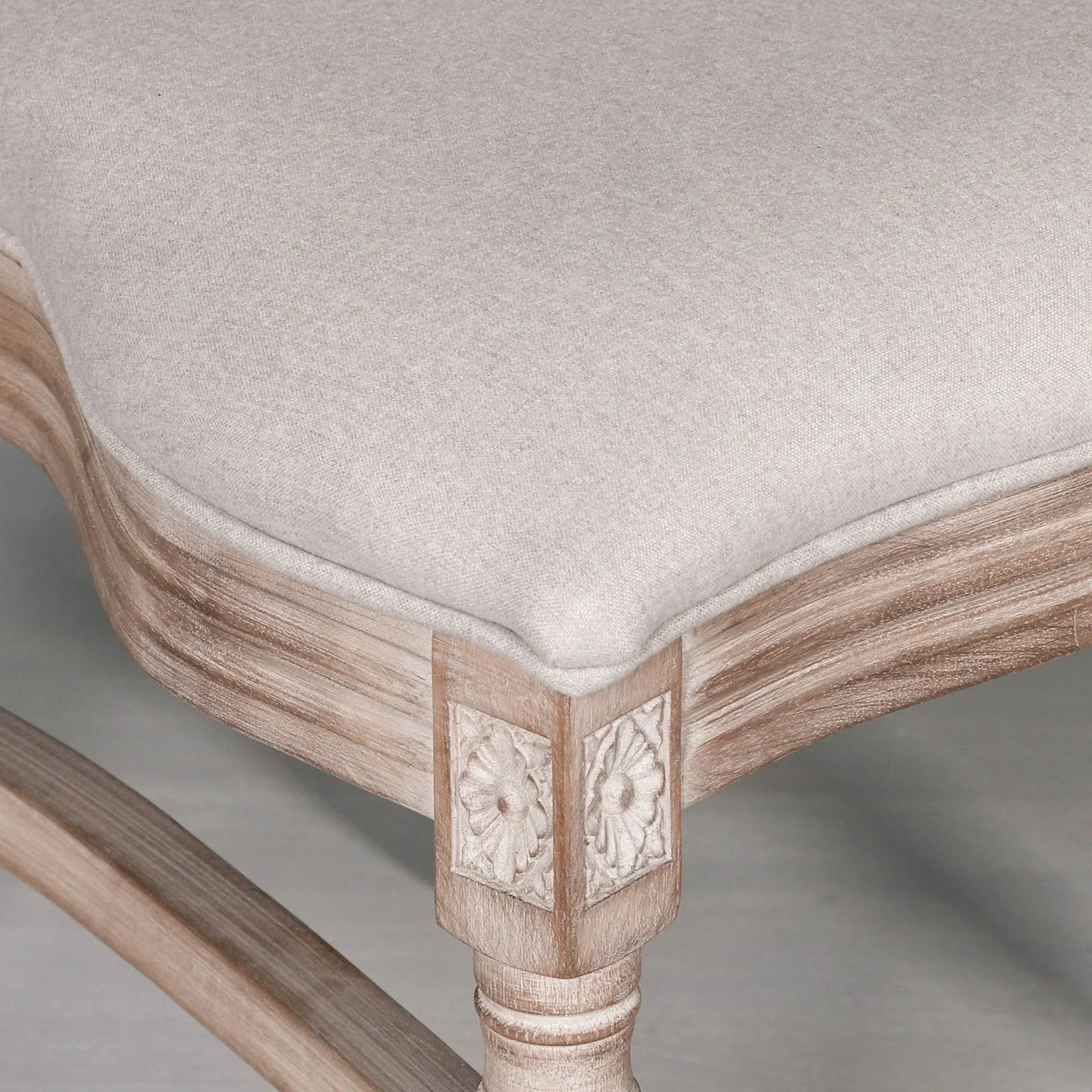 Closeup of upholstered dining chair seat with carved floral wood detail and light fabric