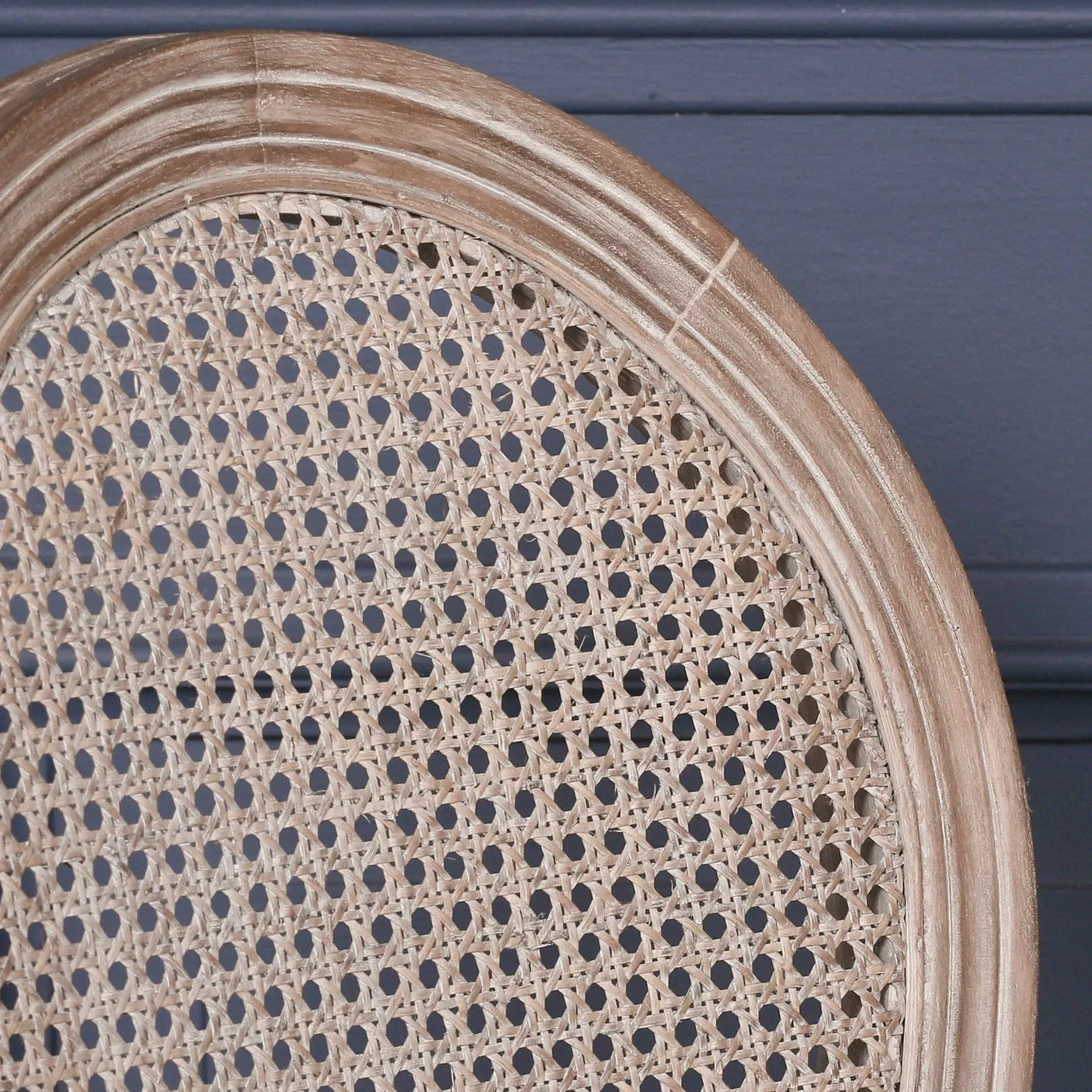 Closeup of natural rattan dining chair backrest with oak wood frame against dark wall