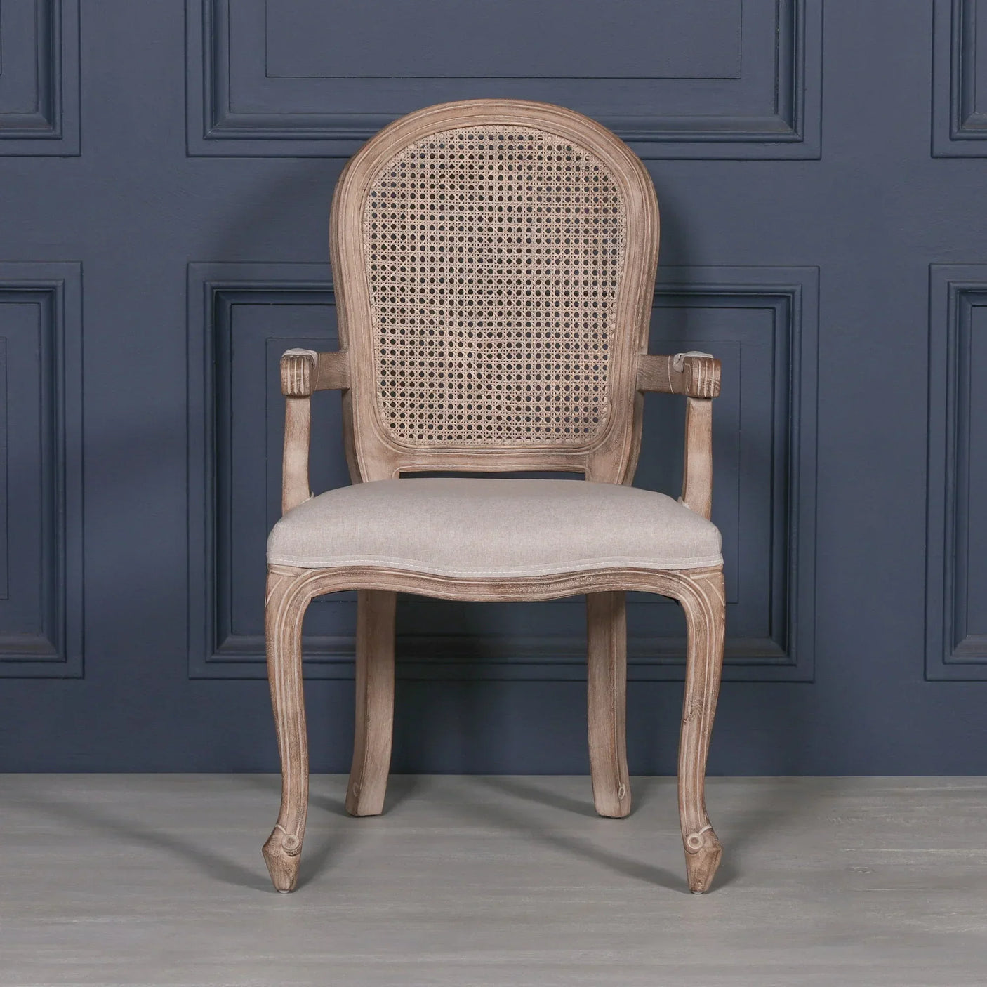 Oak cane back dining chair with upholstered seat and curved arms against navy paneled wall
