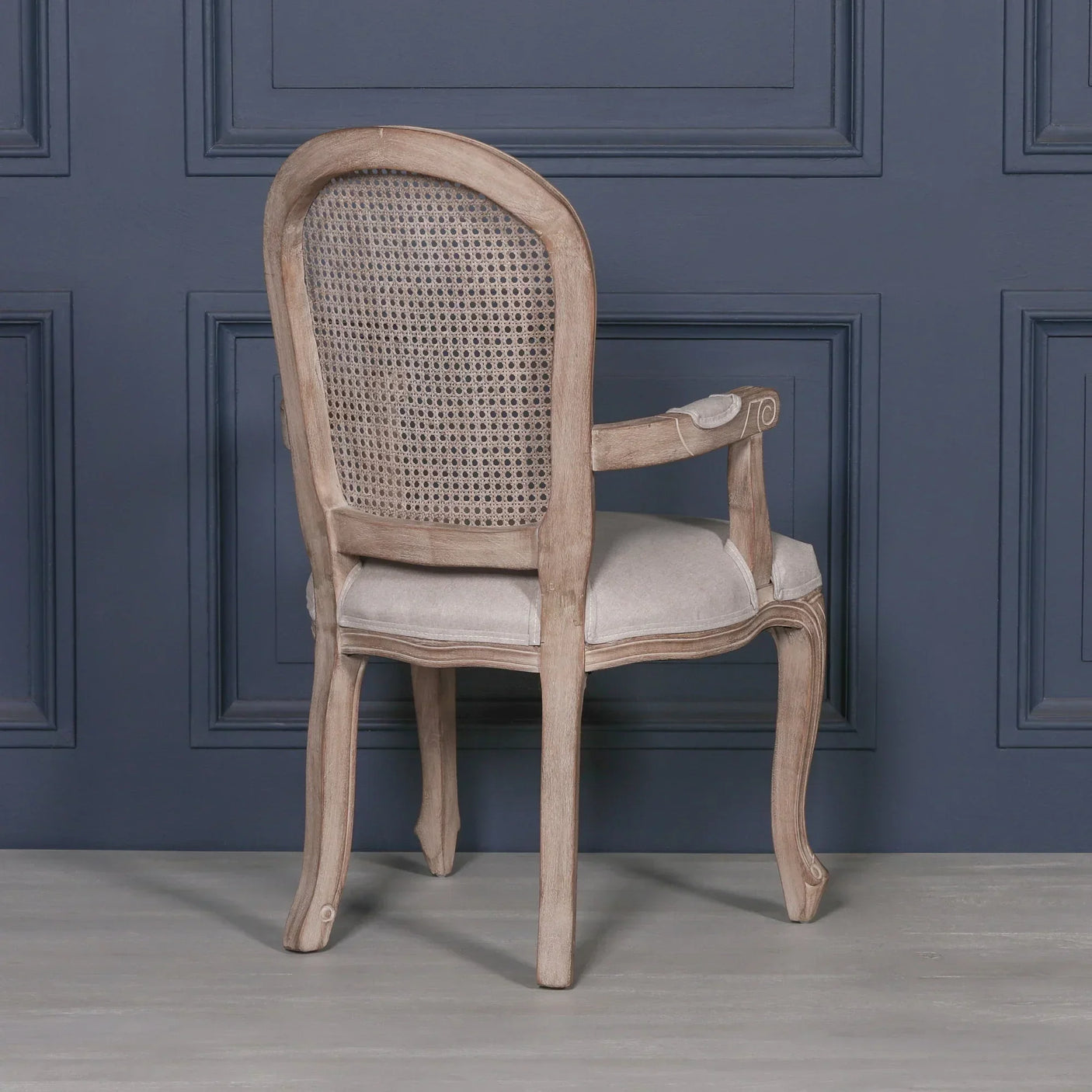 Oak dining chair with upholstered seat and cane backrest, rear view against blue wall