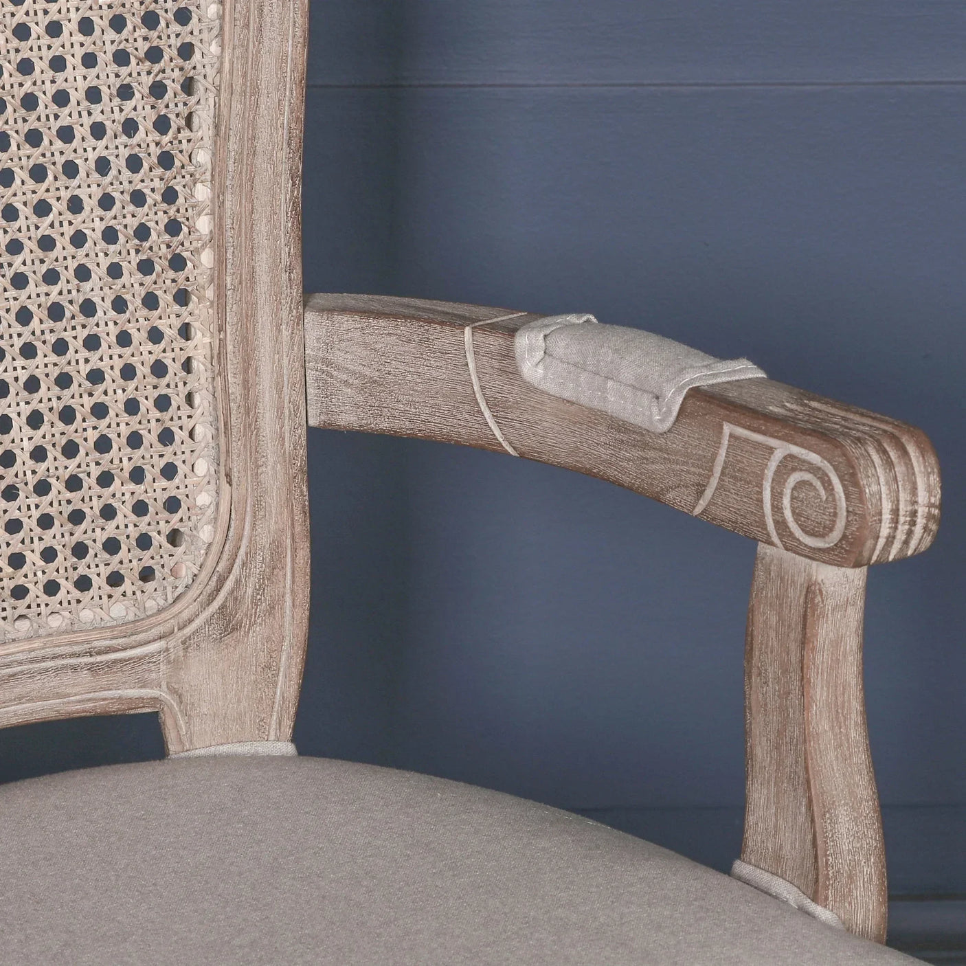 Light wood dining chair with rattan backrest, carved arm detail, and grey fabric seat