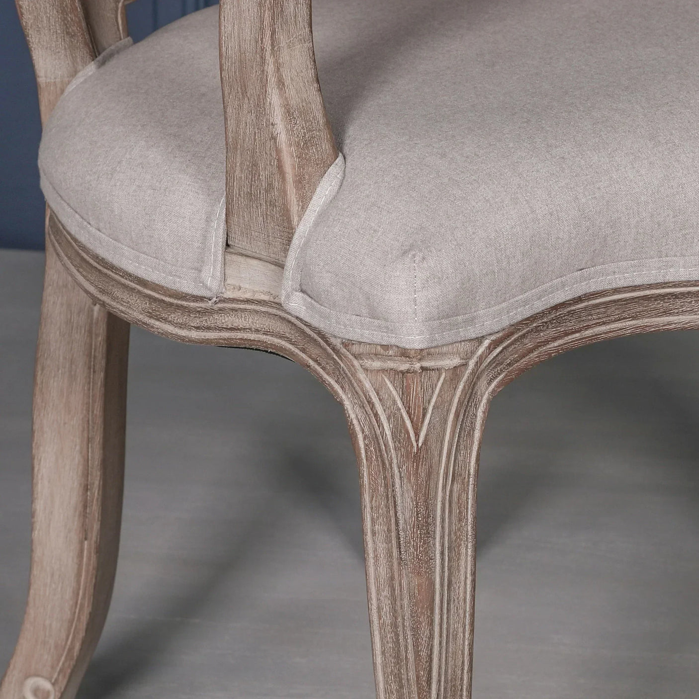 Closeup of wooden dining chair with grey fabric upholstered seat and carved leg detail