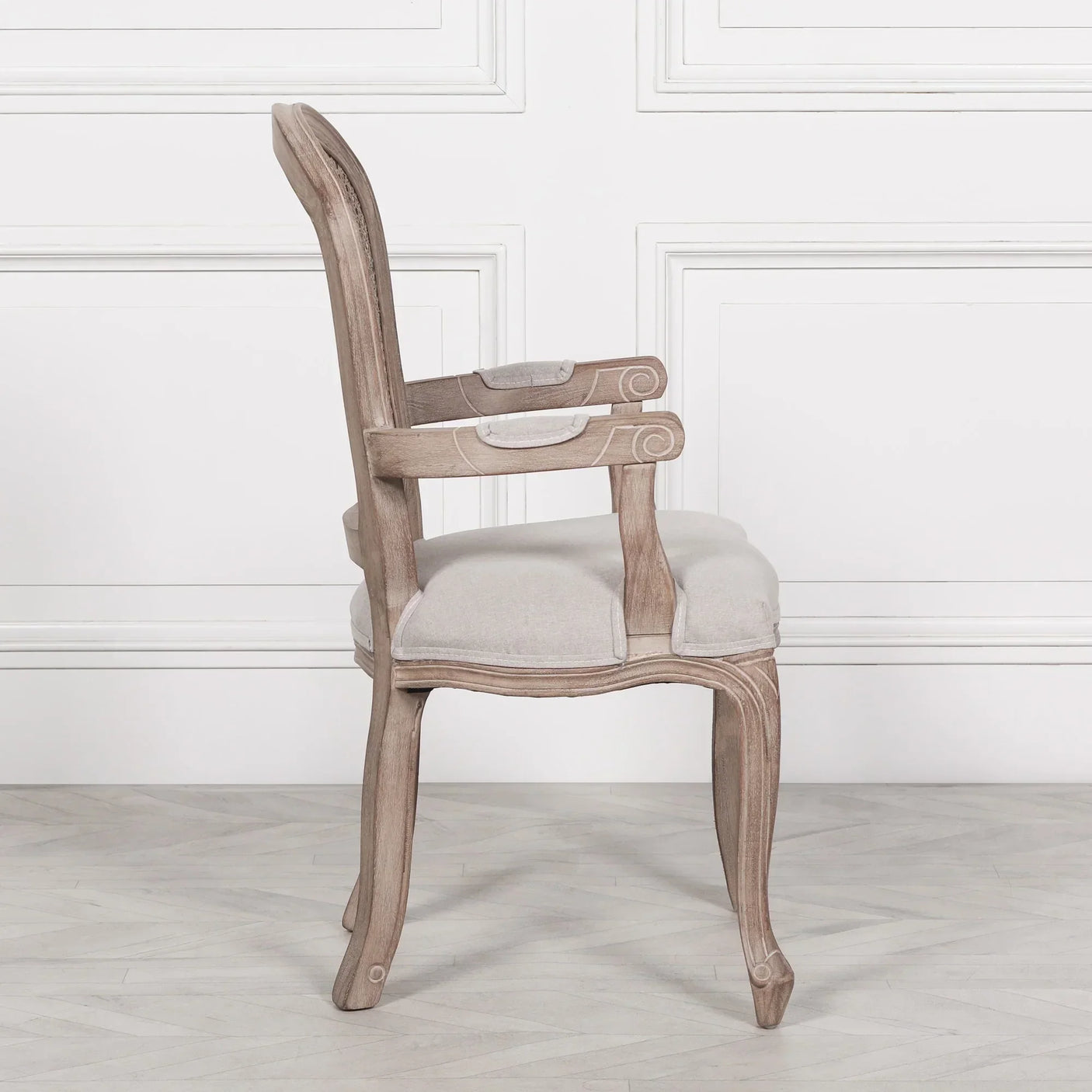 Side view of wooden dining chair with light fabric upholstery and curved armrests