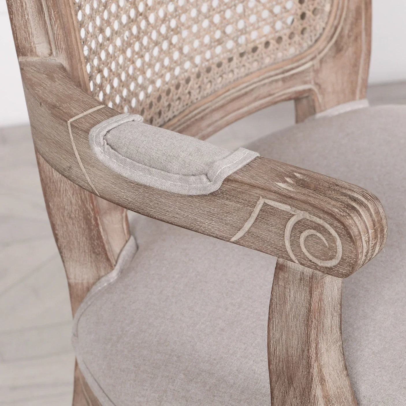 Close view of carved wooden armchair with rattan backrest and light linen upholstery