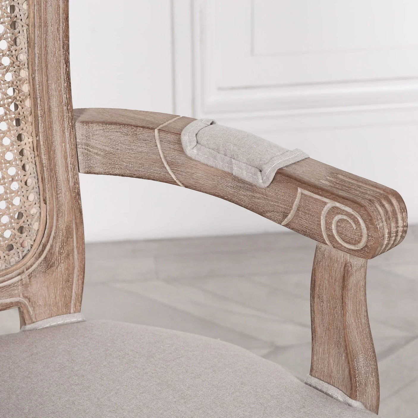 Close up of rattan back dining chair with carved wood armrest and linen seat upholstery