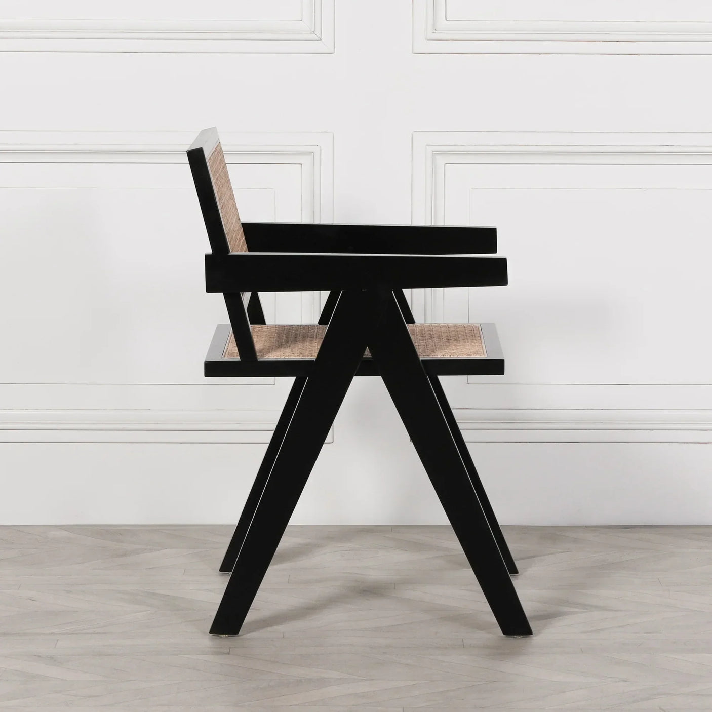 Black wooden dining chair with rattan seat and back, side view on light flooring