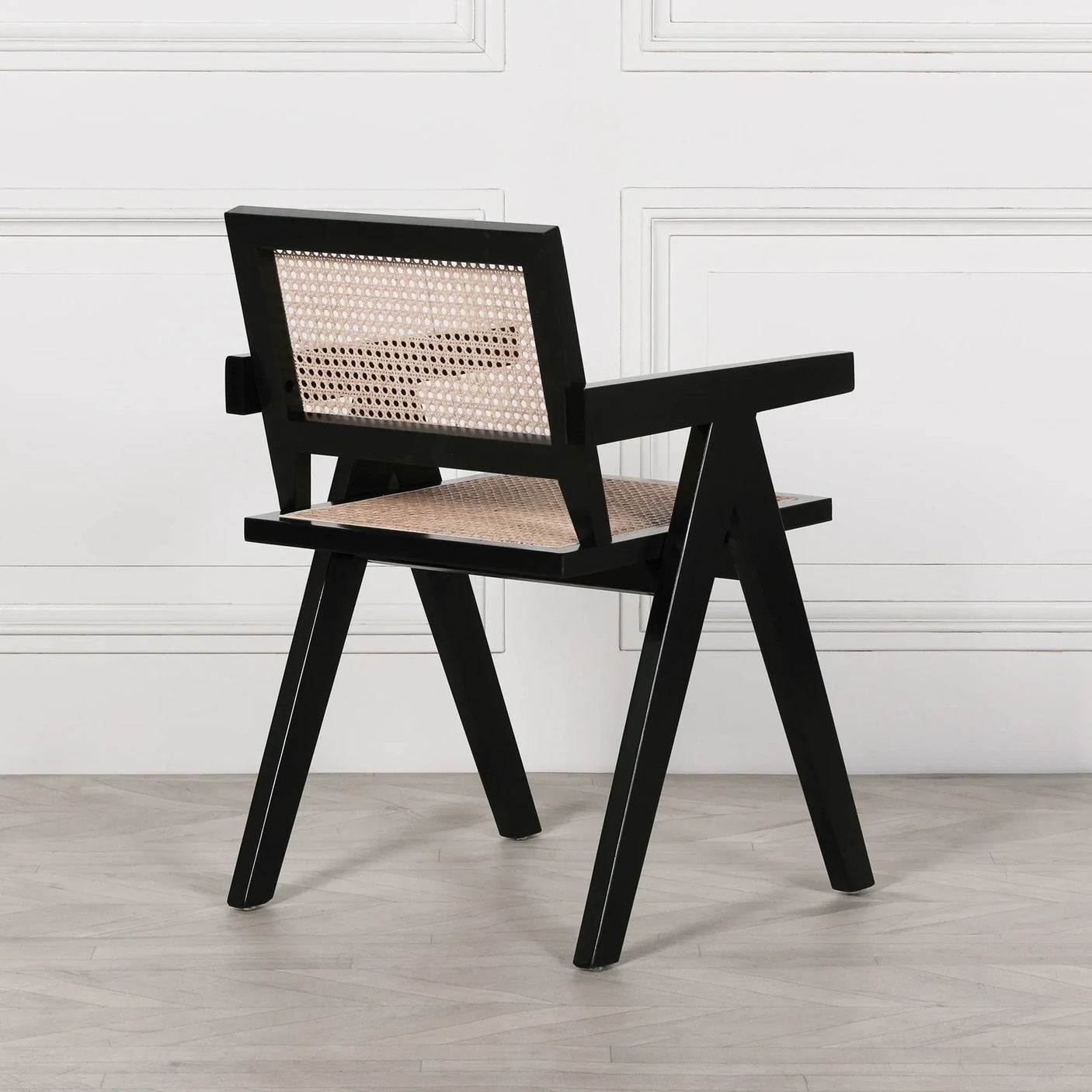 Black wooden dining chair with woven cane seat and backrest on light wood floor