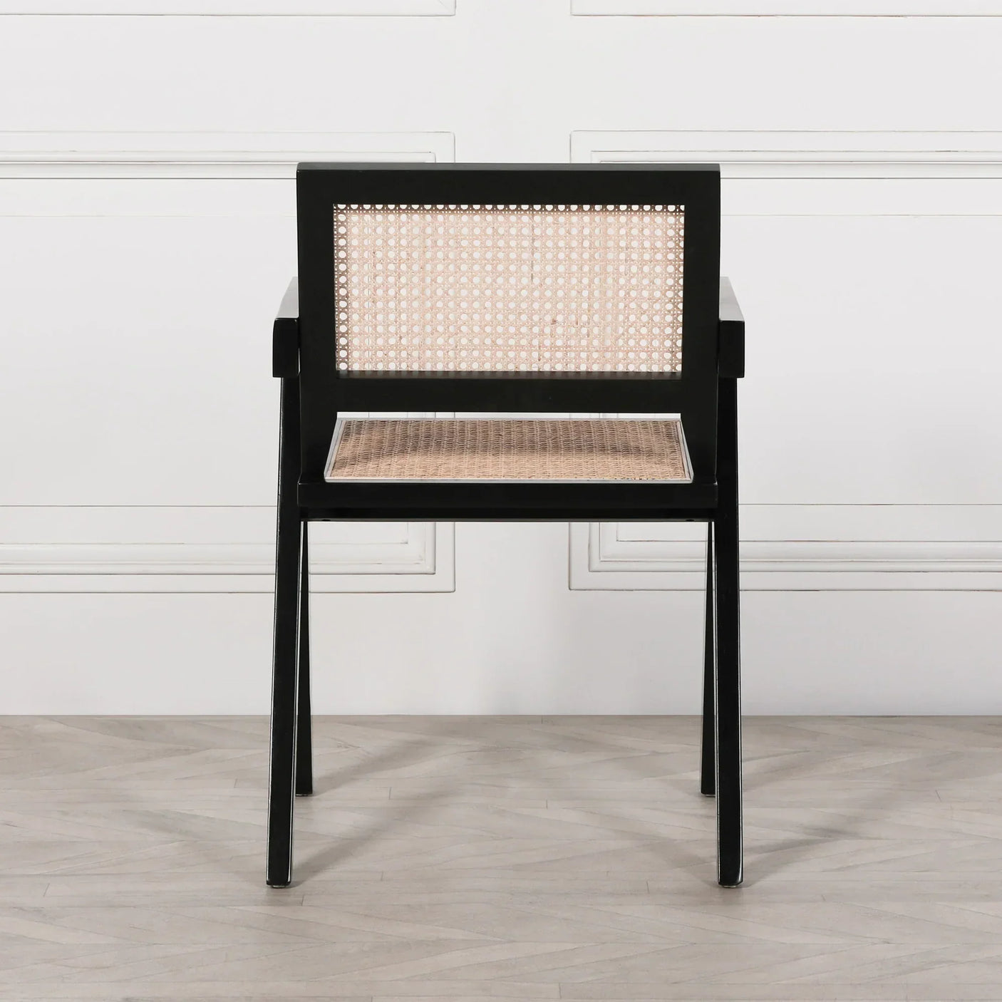Black framed dining chair with rattan seat and backrest on light wood floor