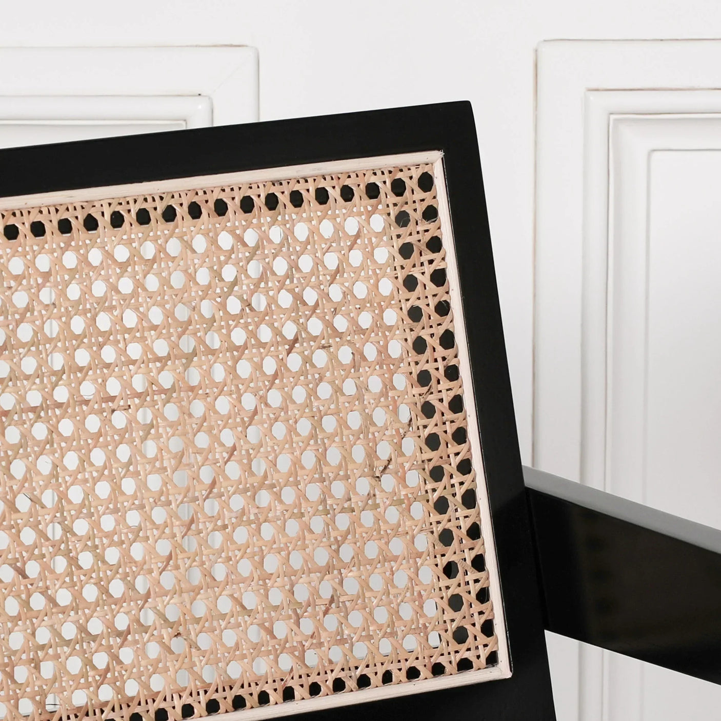 Close detail of rattan chair backrest with black wood frame against white panel wall