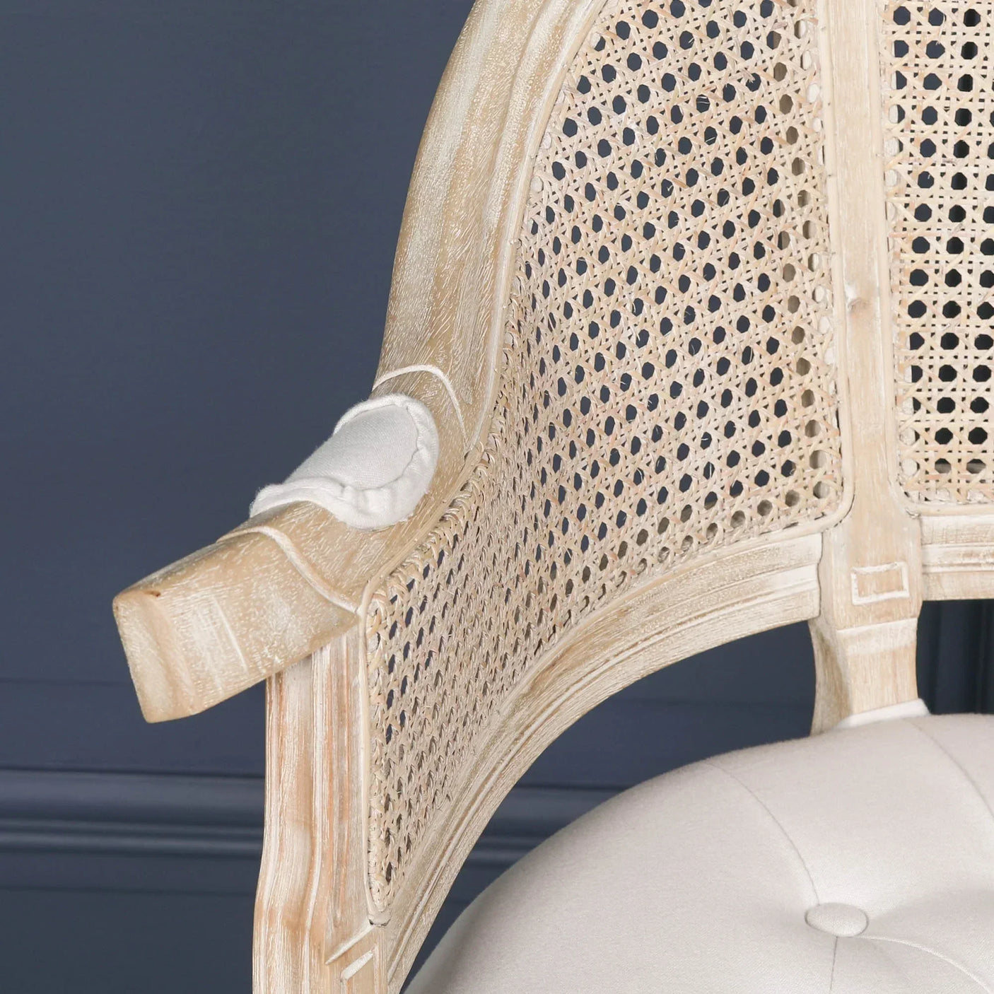 Close-up of rattan armchair with light wood frame and tufted cream cushion