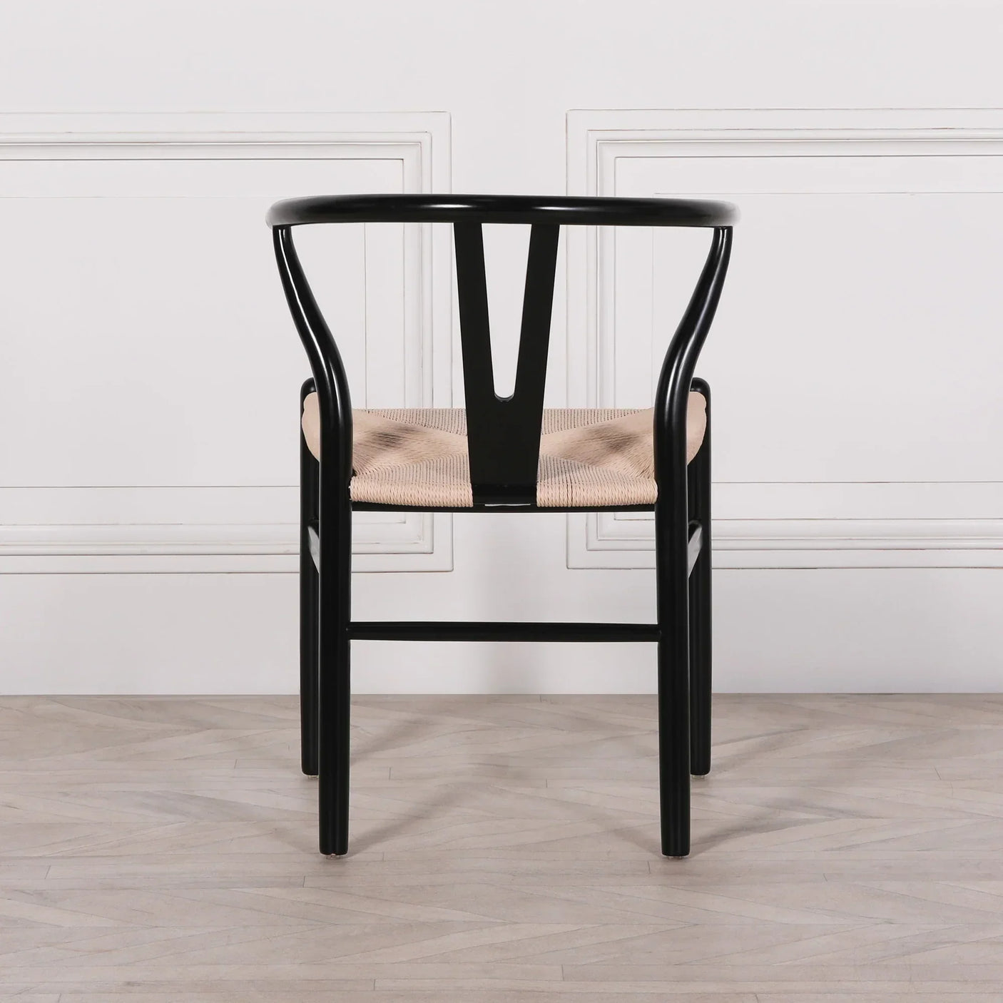 Black wooden dining chair with curved back and woven seat on light wood floor