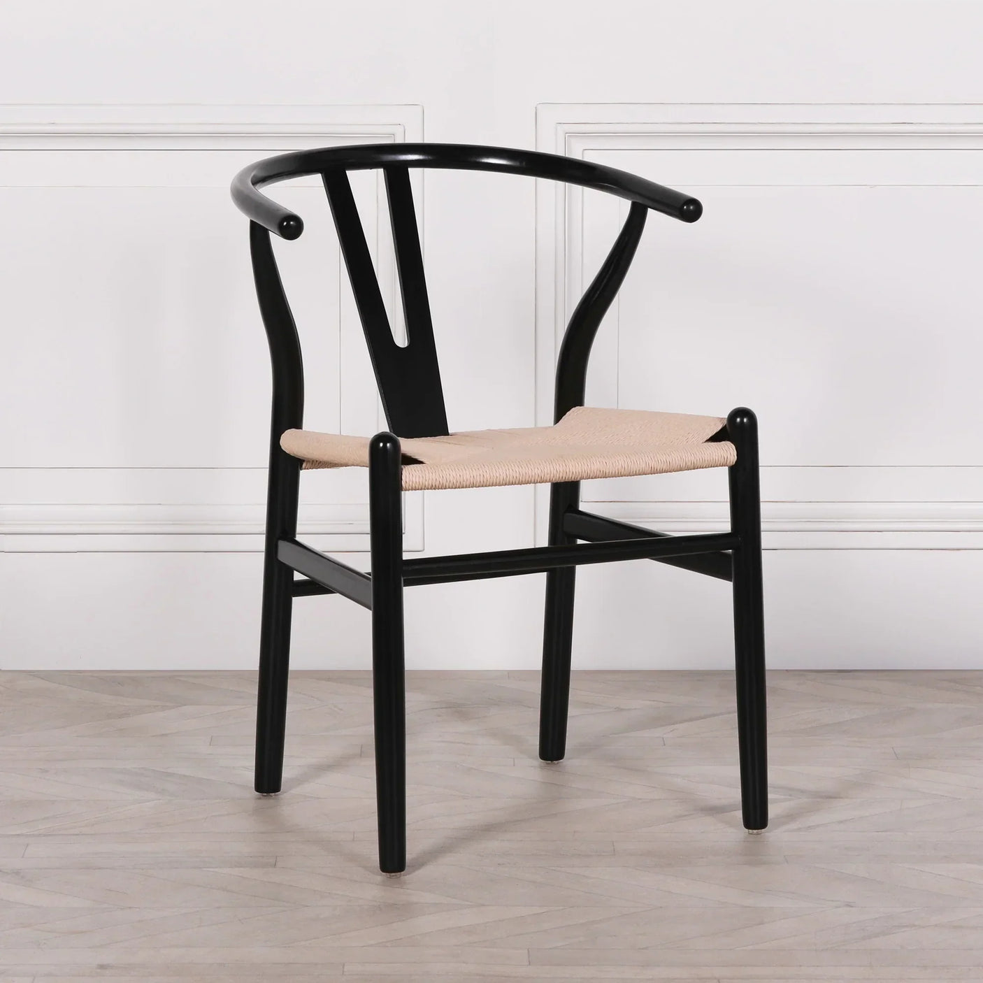 Black wishbone dining chair with natural woven seat against white panel wall