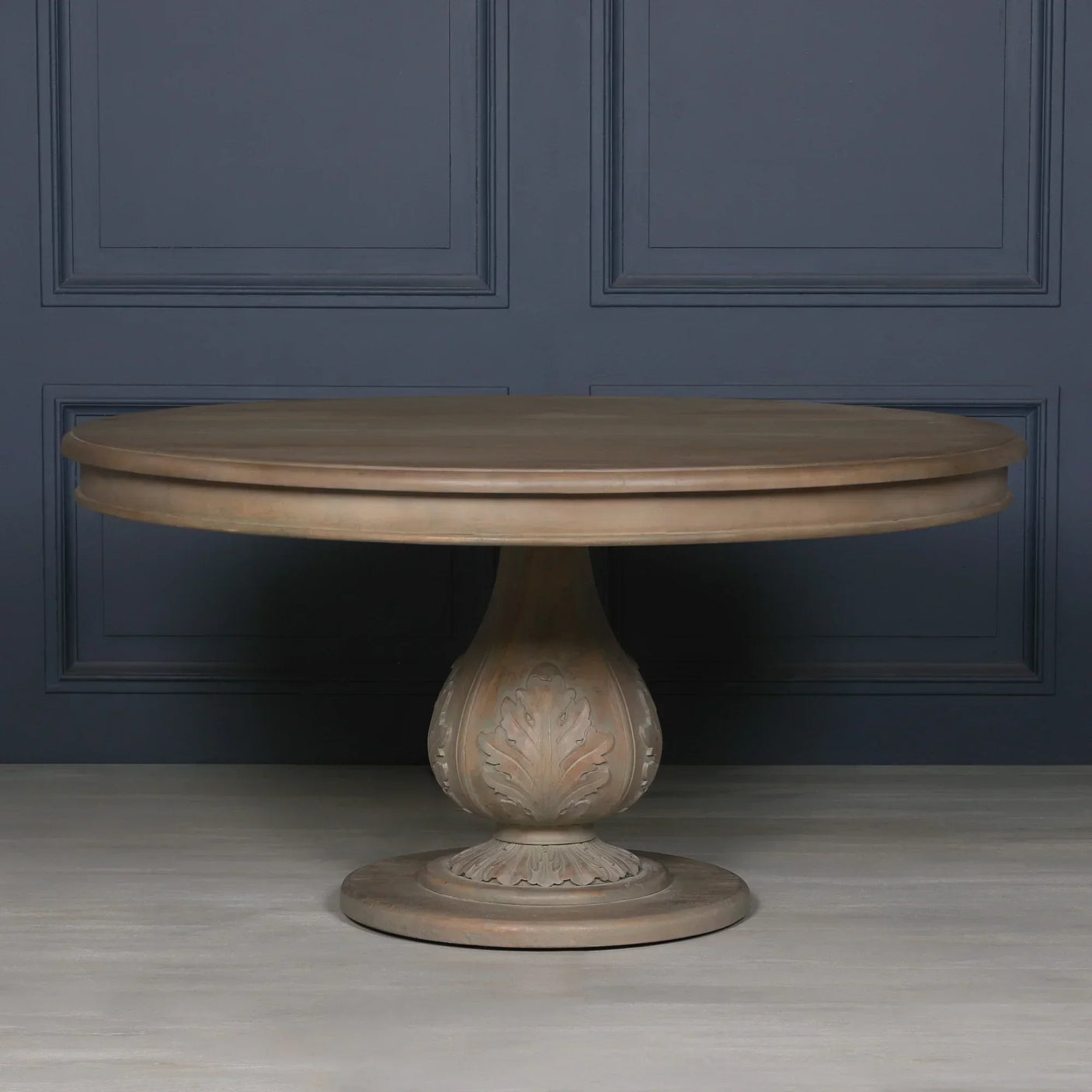 Round wooden dining table with carved pedestal base against dark paneled wall