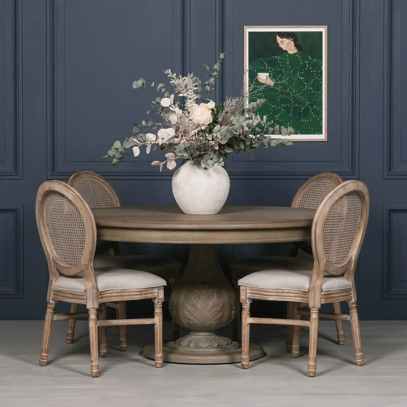 Round oak dining table with carved pedestal base and four rattan back chairs, floral centerpiece
