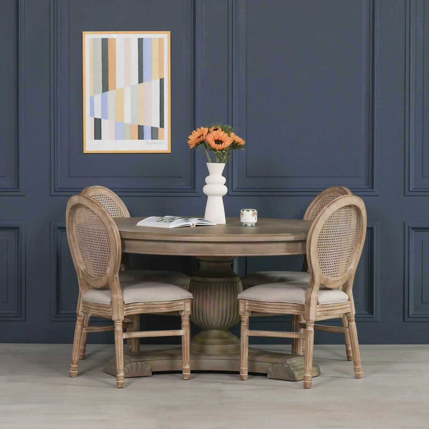 Round wooden dining table with four rattan back chairs and vase of flowers