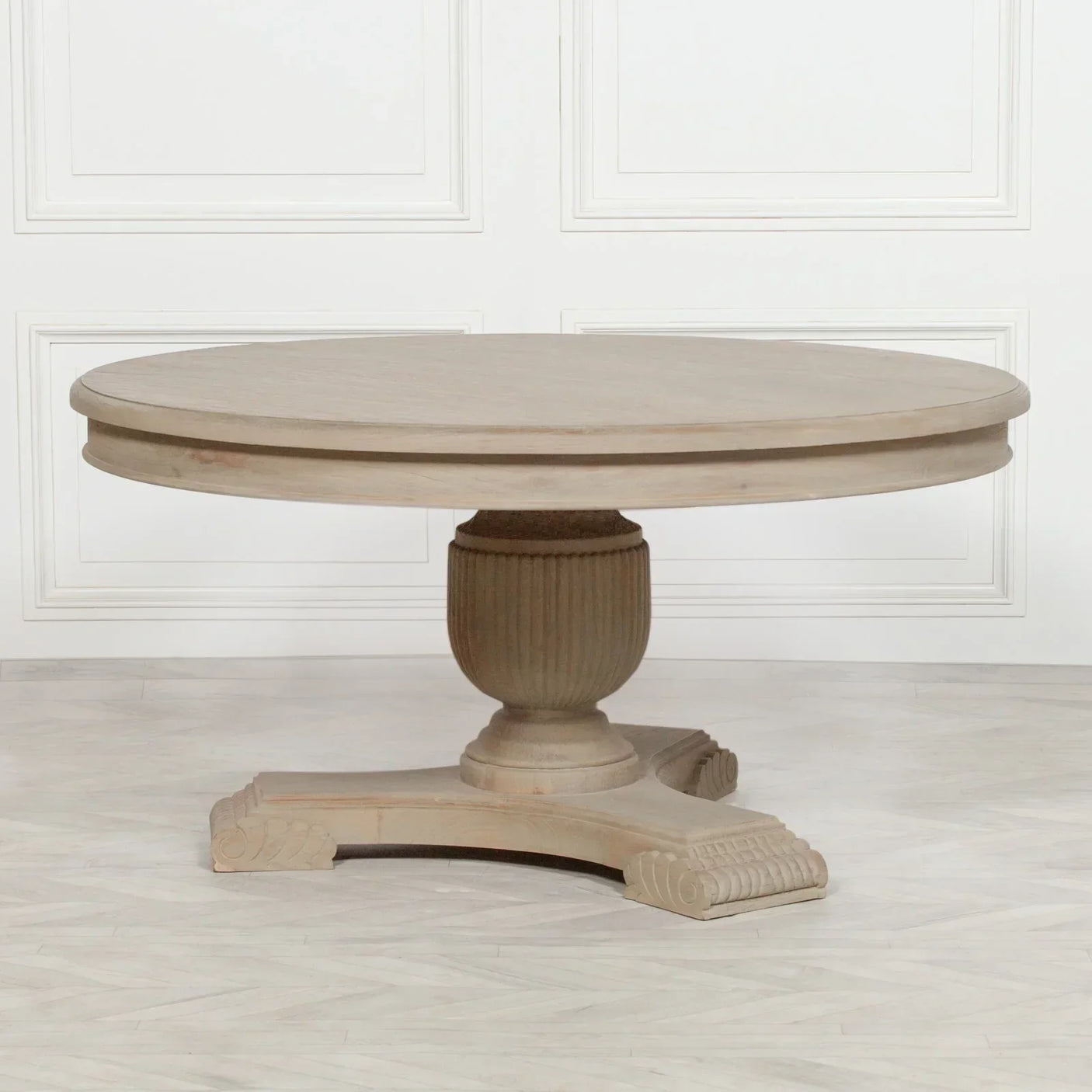 Round wooden dining table with pedestal base on light wood floor