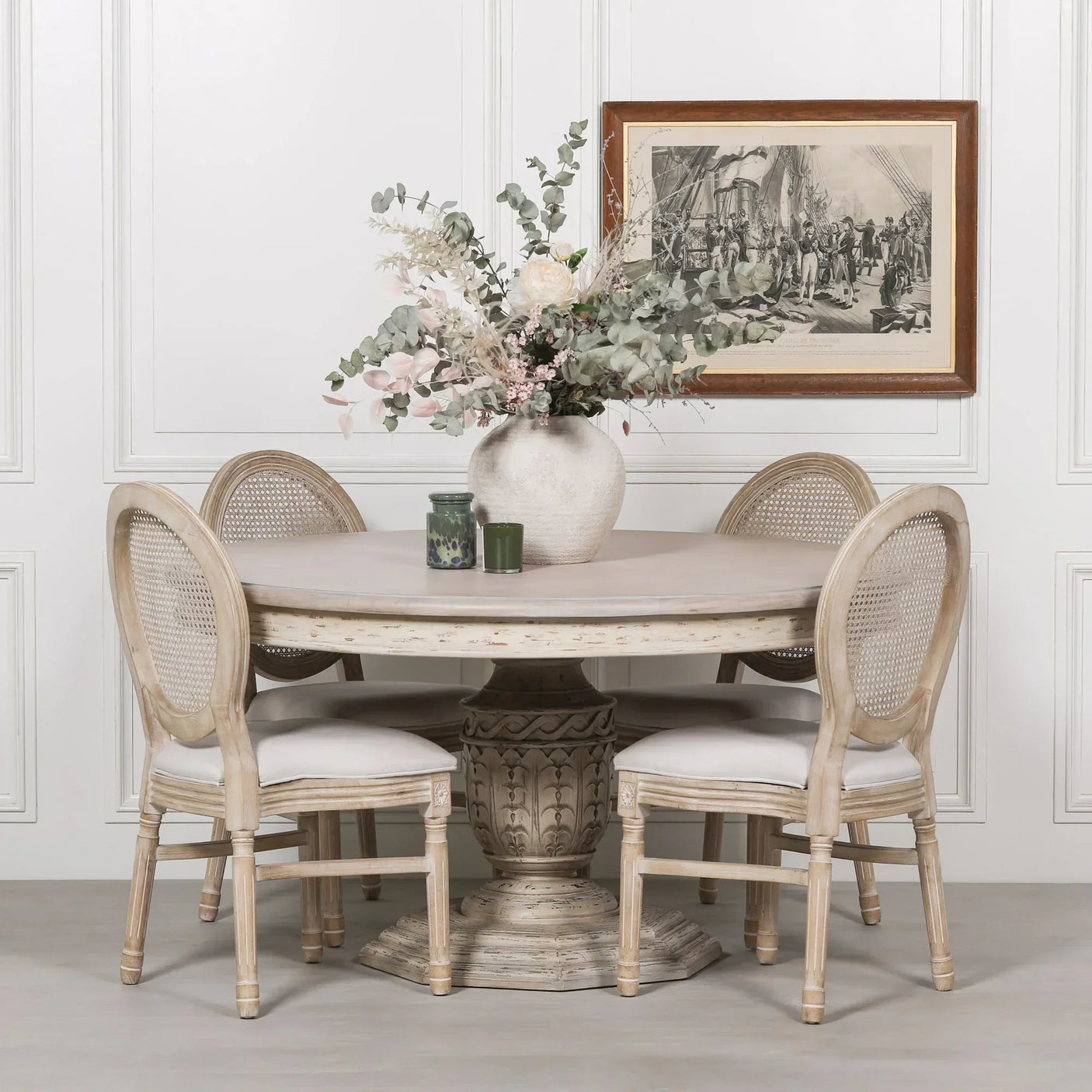 Round wooden dining table with pedestal base and four upholstered chairs in neutral tones