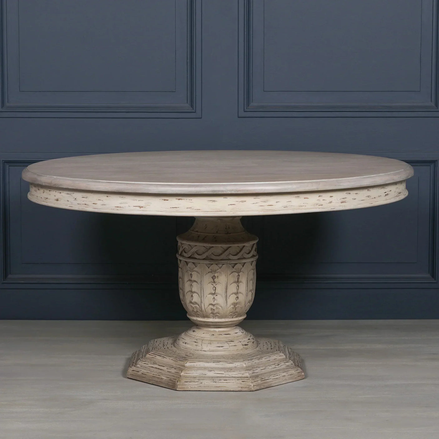 Round wooden dining table with carved pedestal base and distressed finish