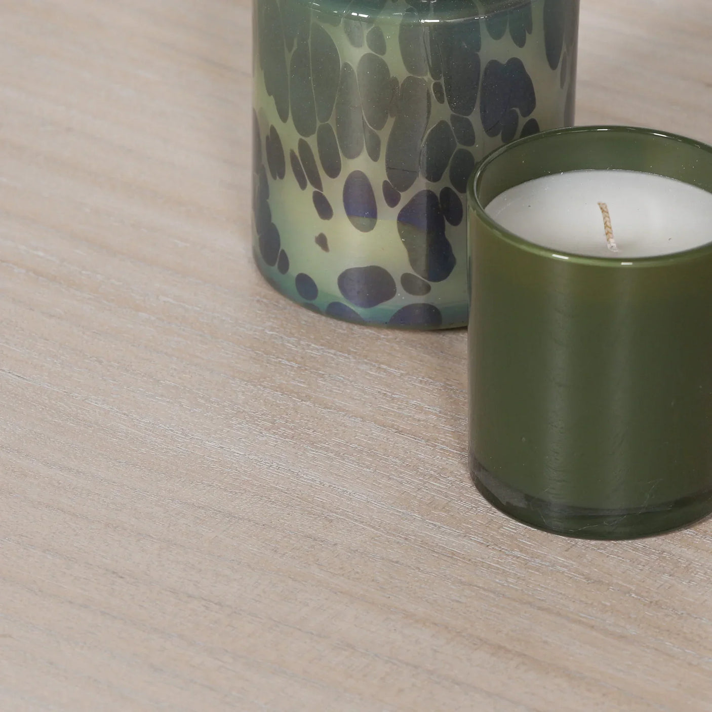 Green glass candle holder and spotted glass candle on light wood table