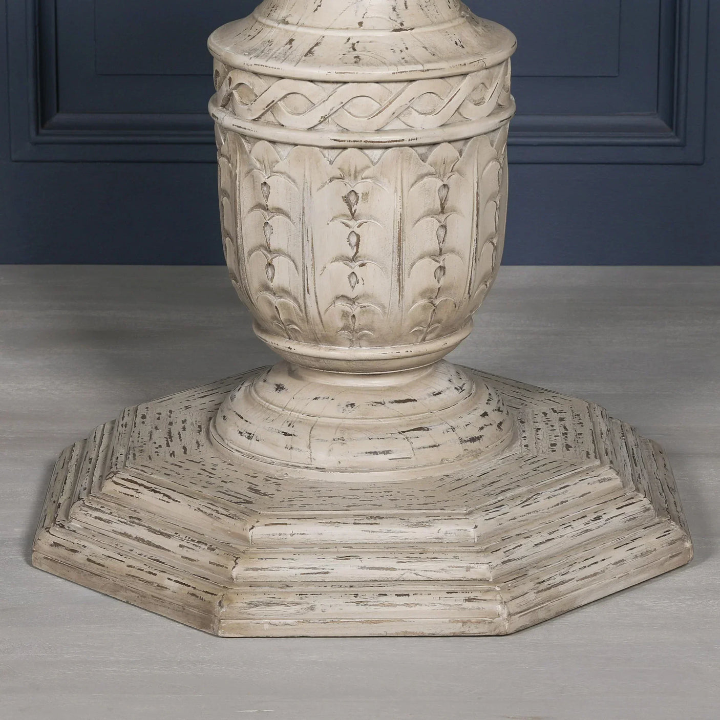 Distressed wood dining table pedestal base with carved detailing on grey floor