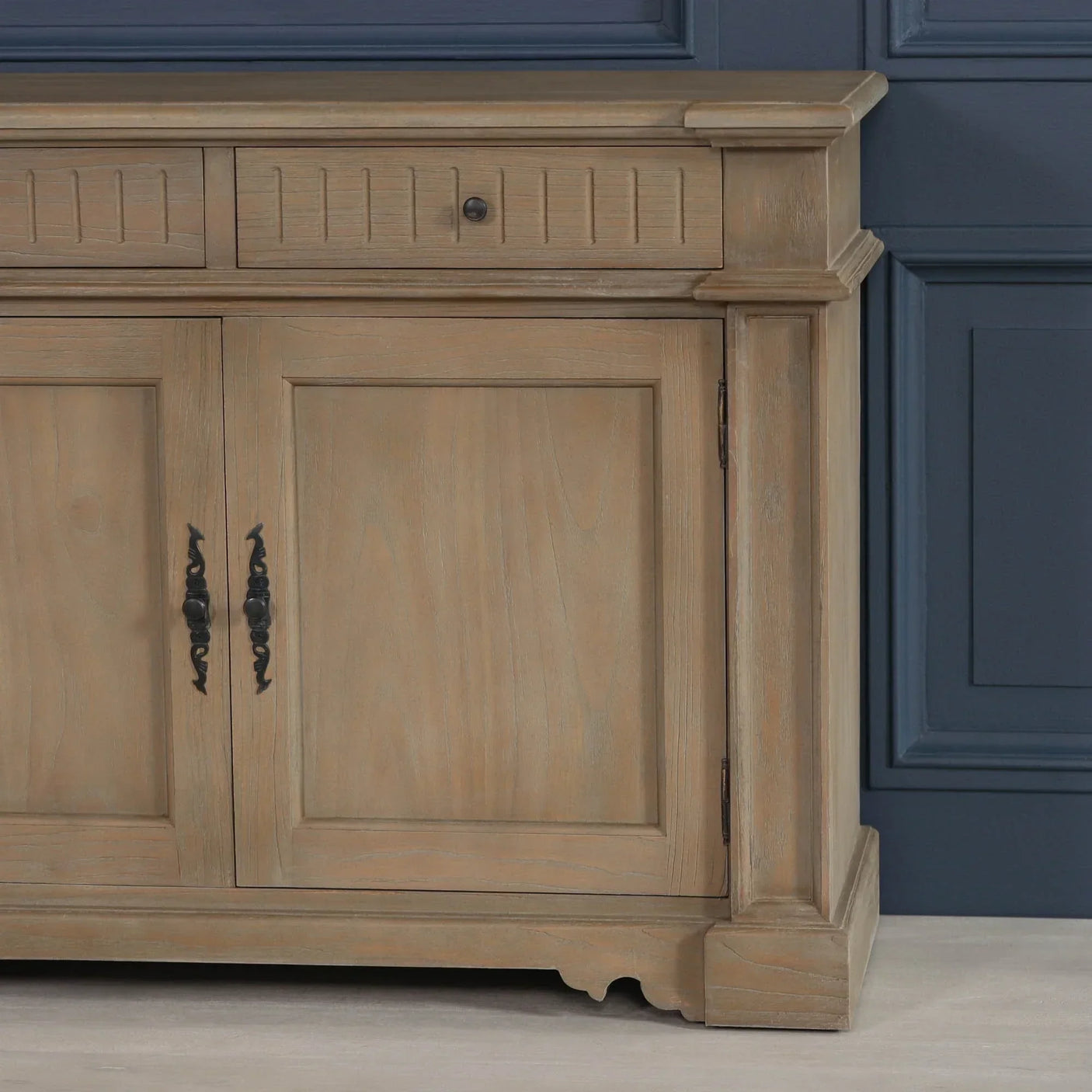Oak sideboard with black metal handles and panelled drawers against blue wall