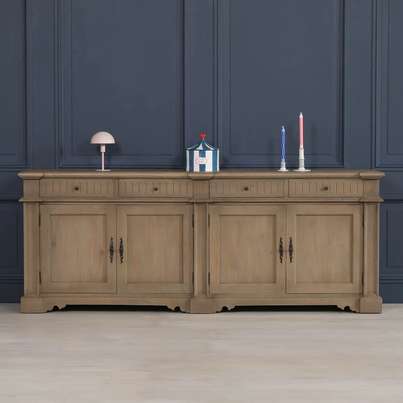 Large oak sideboard cabinet with four doors, drawers, and decorative handles against blue wall