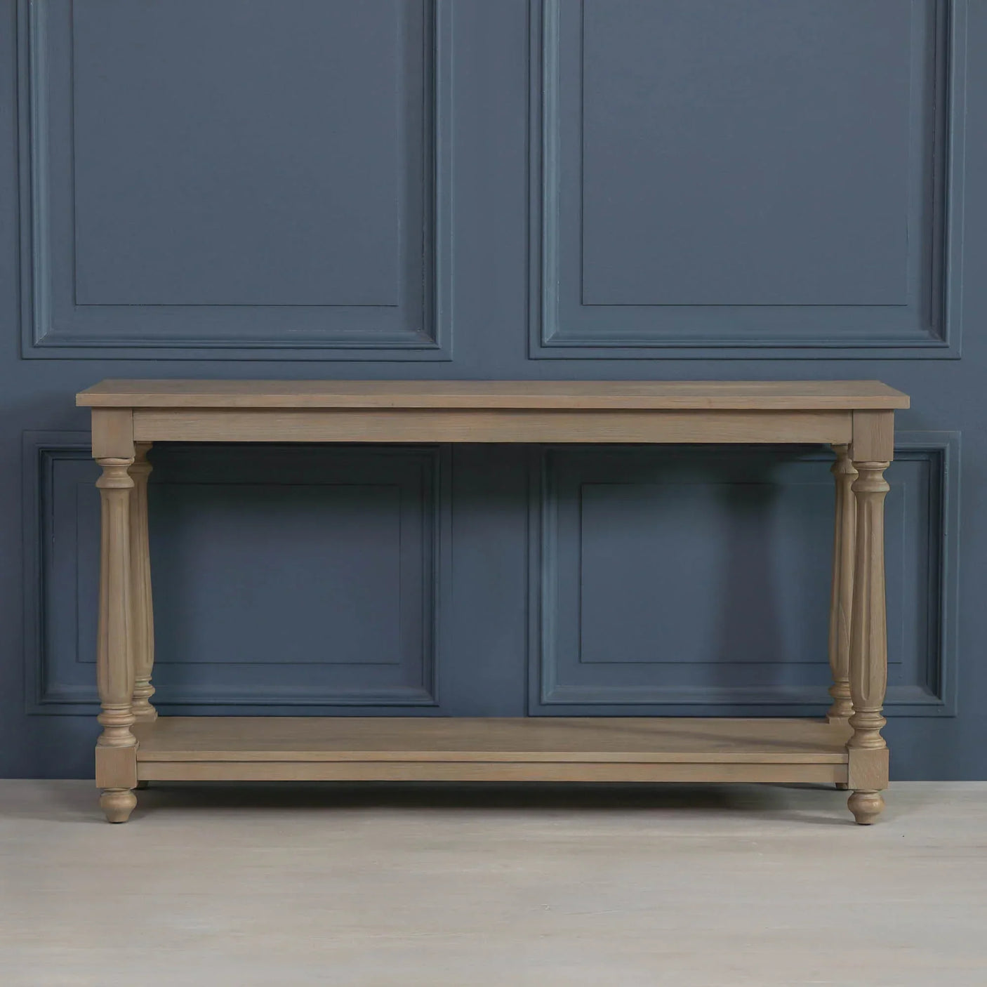 Wooden console table with lower shelf and turned legs against blue paneled wall