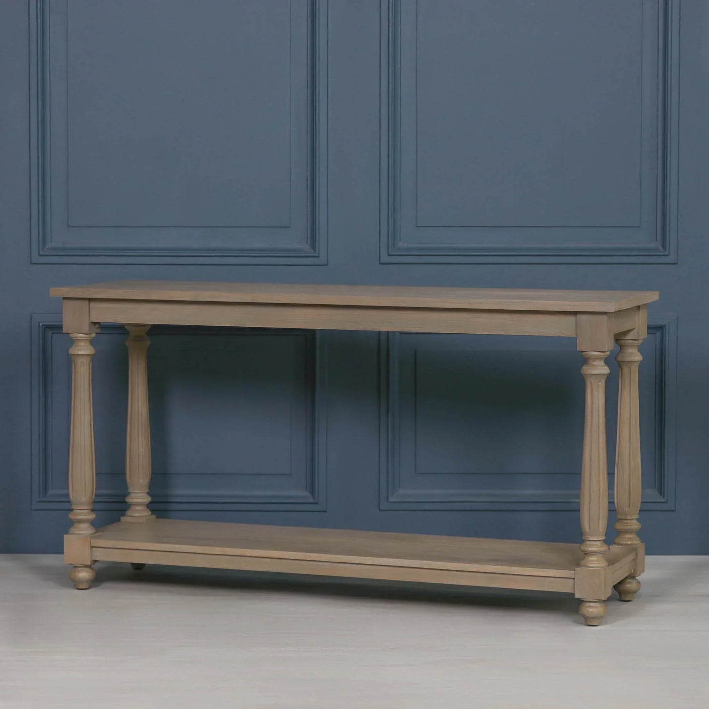 Oak console table with turned legs and lower shelf against blue paneled wall