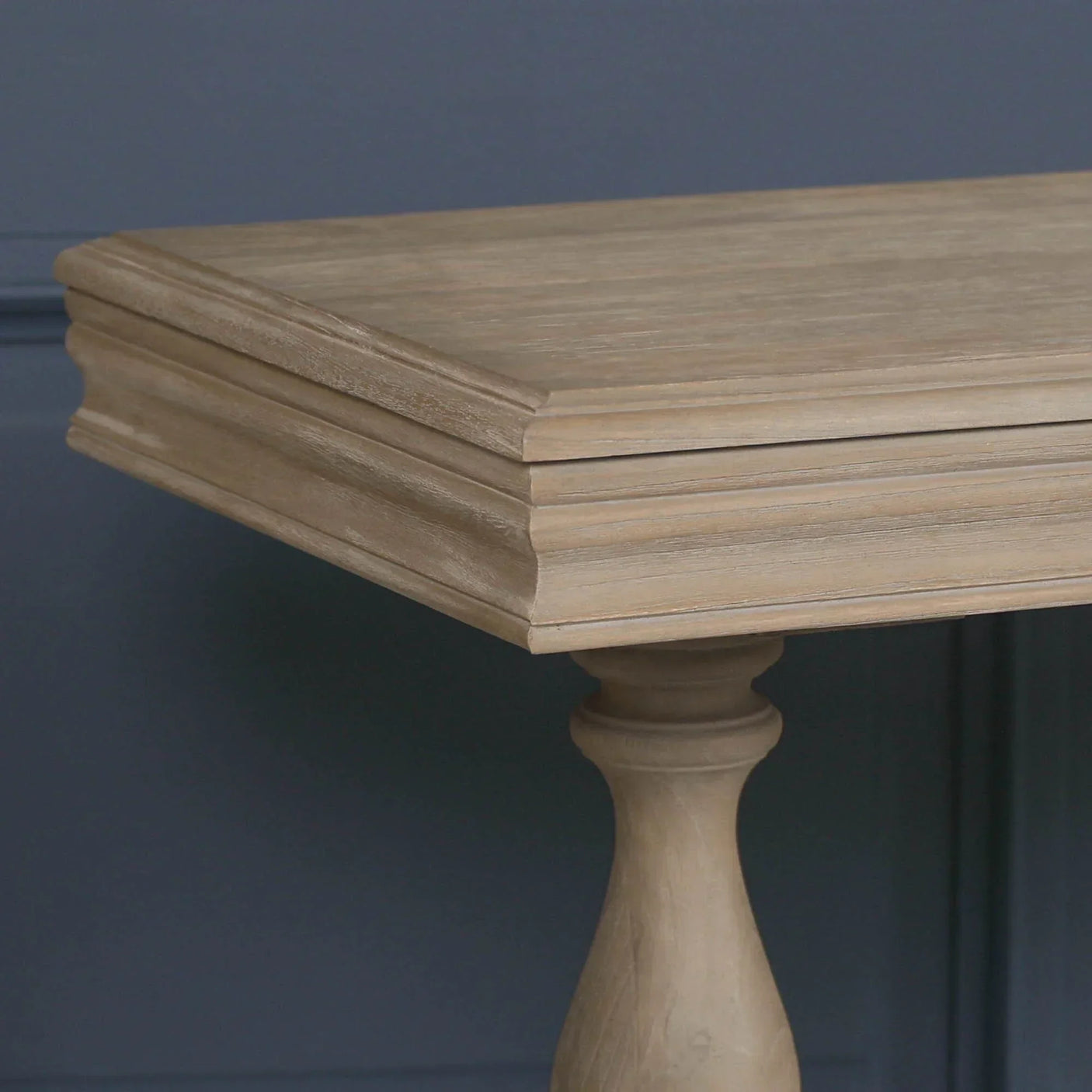 Close view of oak dining table edge with turned wooden leg against dark wall
