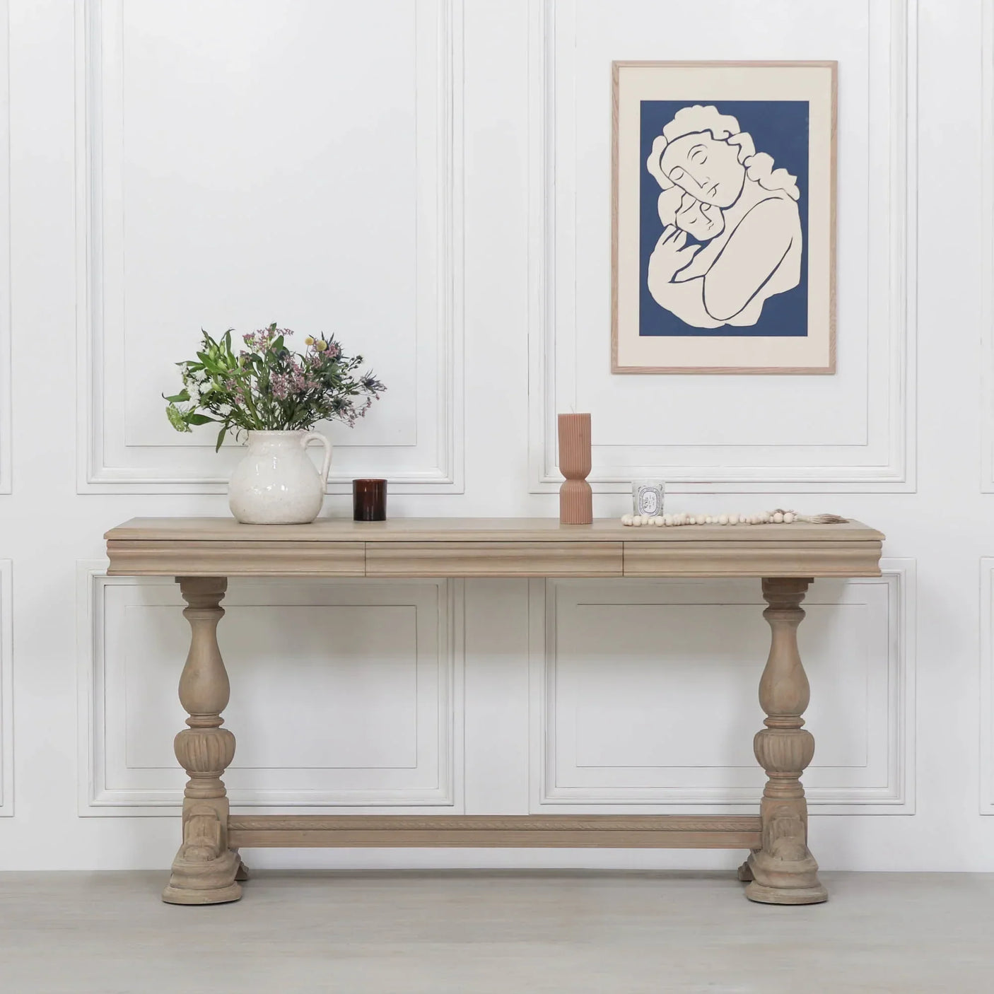 Wood console table with turned legs, floral jug, and decorative items in a white panelled room