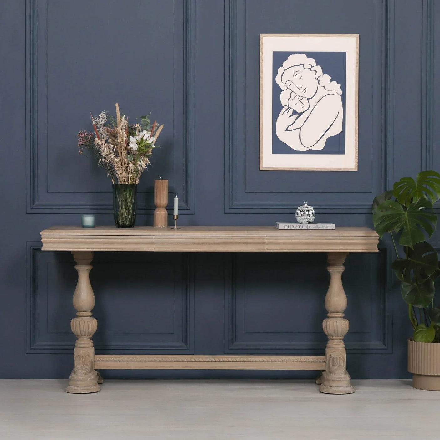 Natural wood console table with carved legs against blue wall, decorated with vases and books