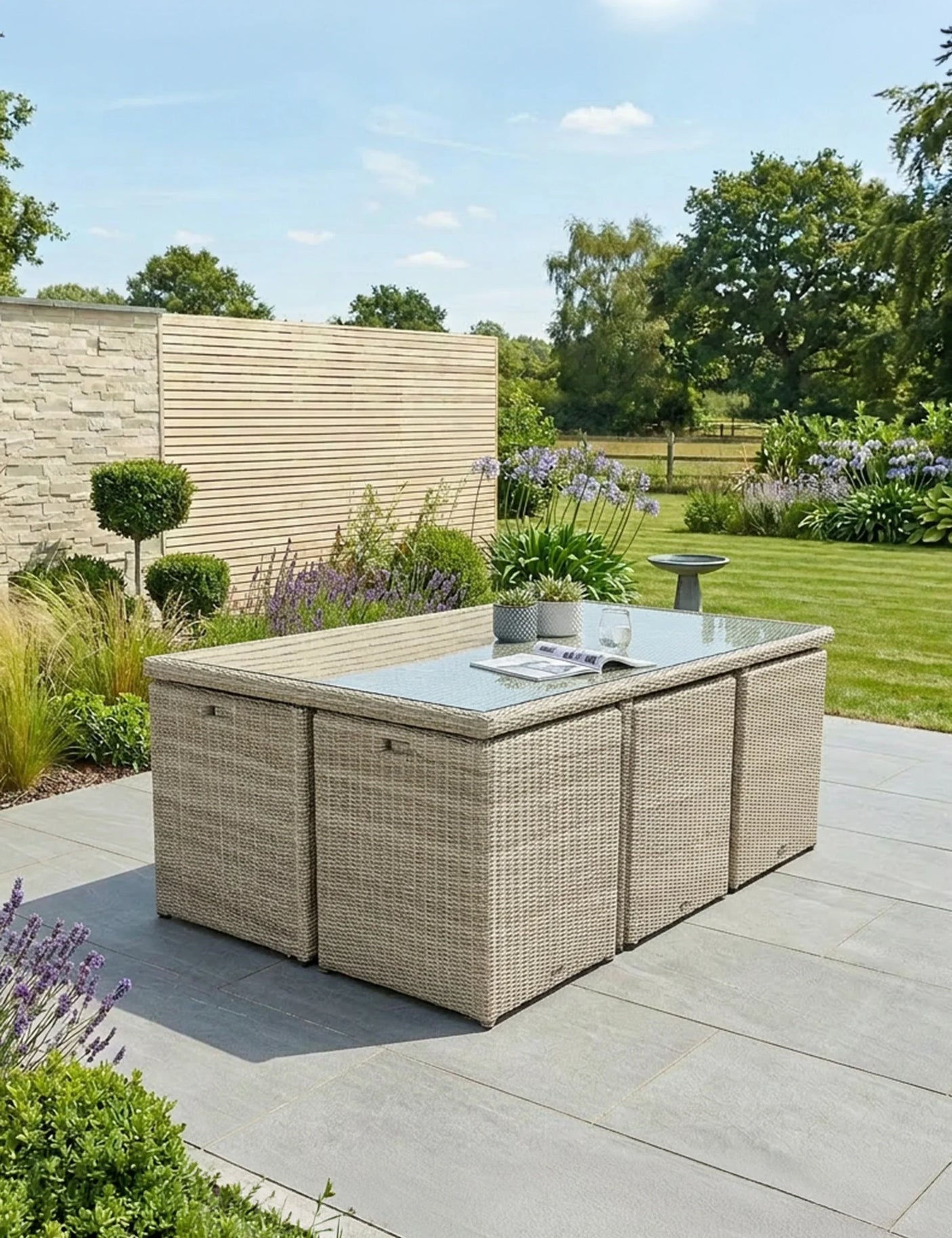Beige rattan outdoor dining set with glass-top table and stools on patio in garden