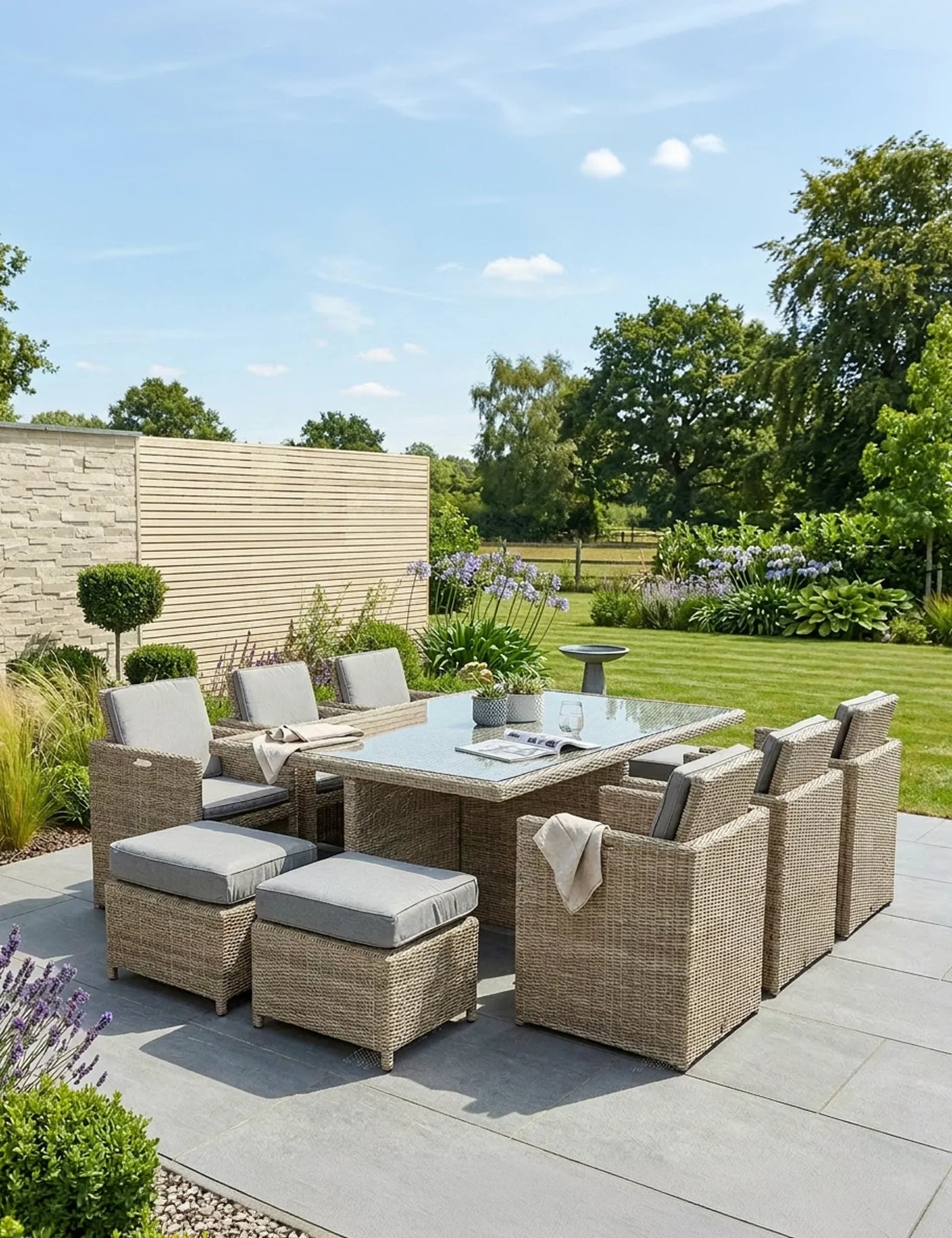 Rattan outdoor dining set with glass table, cushioned chairs and stools on a patio garden