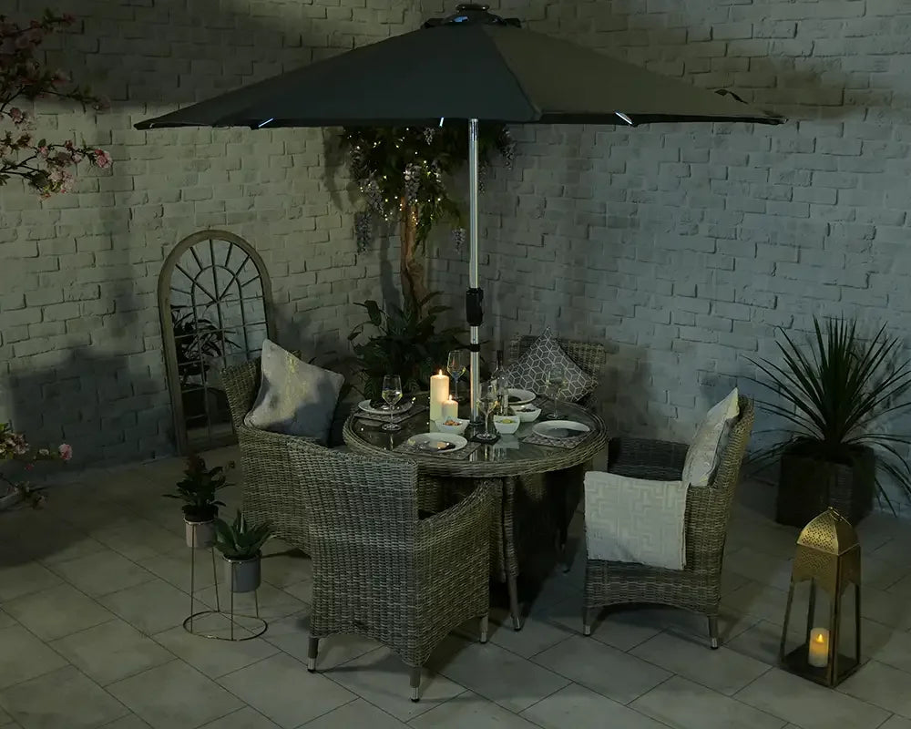 Rattan garden dining set with four chairs, round table, and parasol on tiled patio at night