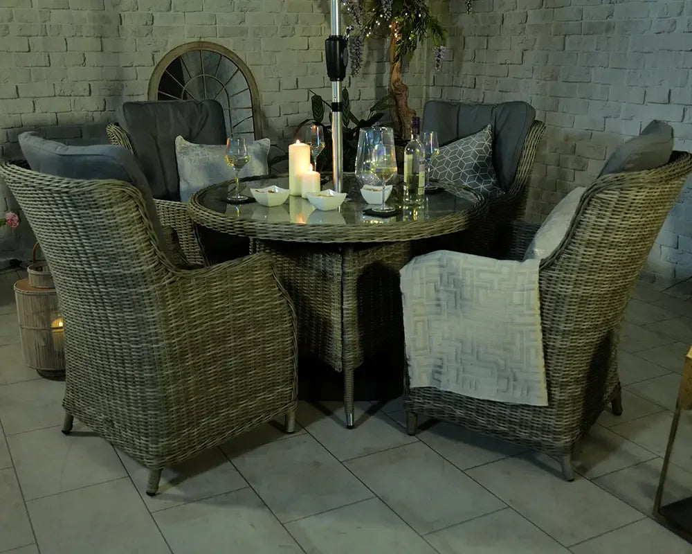Rattan dining set with four cushioned chairs and round glass table arranged indoors