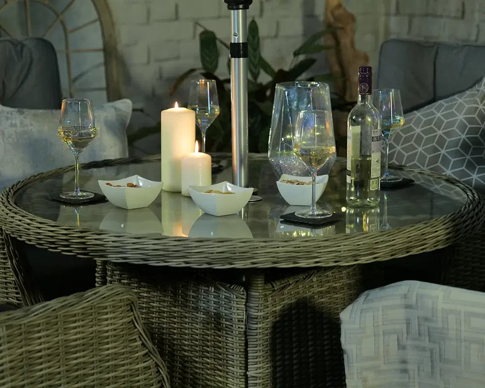 Round rattan garden dining table with glass top, wine glasses, candles and snacks
