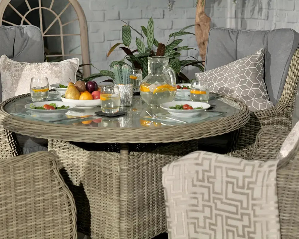 Round rattan garden dining set with glass top, grey cushions, fruit and drinks on table